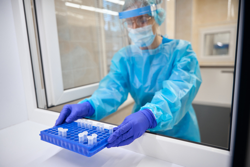 Laboratory assistant in protective equipment holds a tray with test tubes
