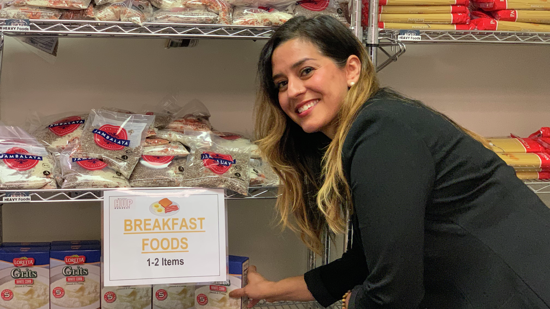 Sofia Carreno smiles while stocking a pantry shelf labeled "Breakfast foods"