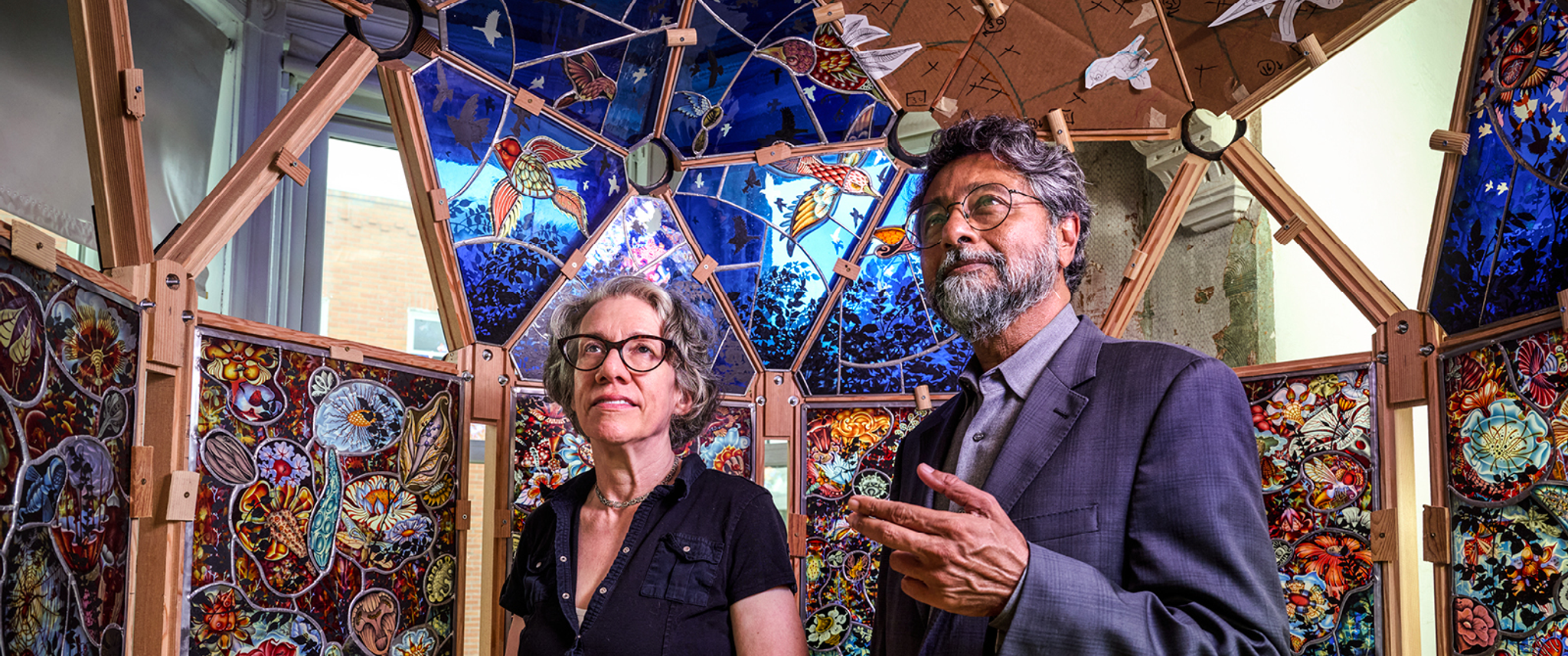 Artist Judith Schaechter and Neurology professor Anjan K. Chatterjee, MD, stand inside a dome of colored glass panels that Schaechter is building