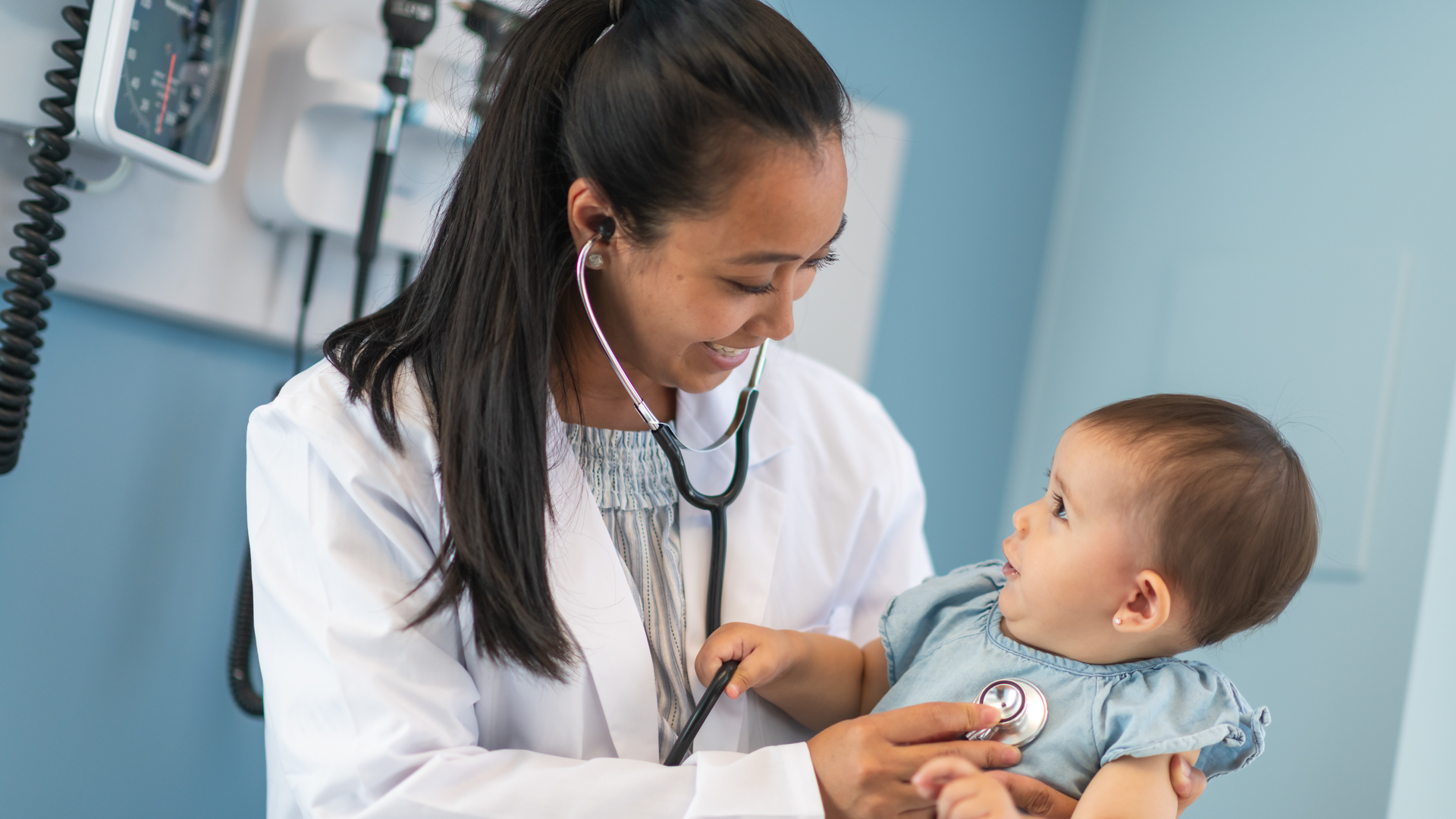 A pediatric doctor holding her infant patient and listening to her heart with a stethoscope.