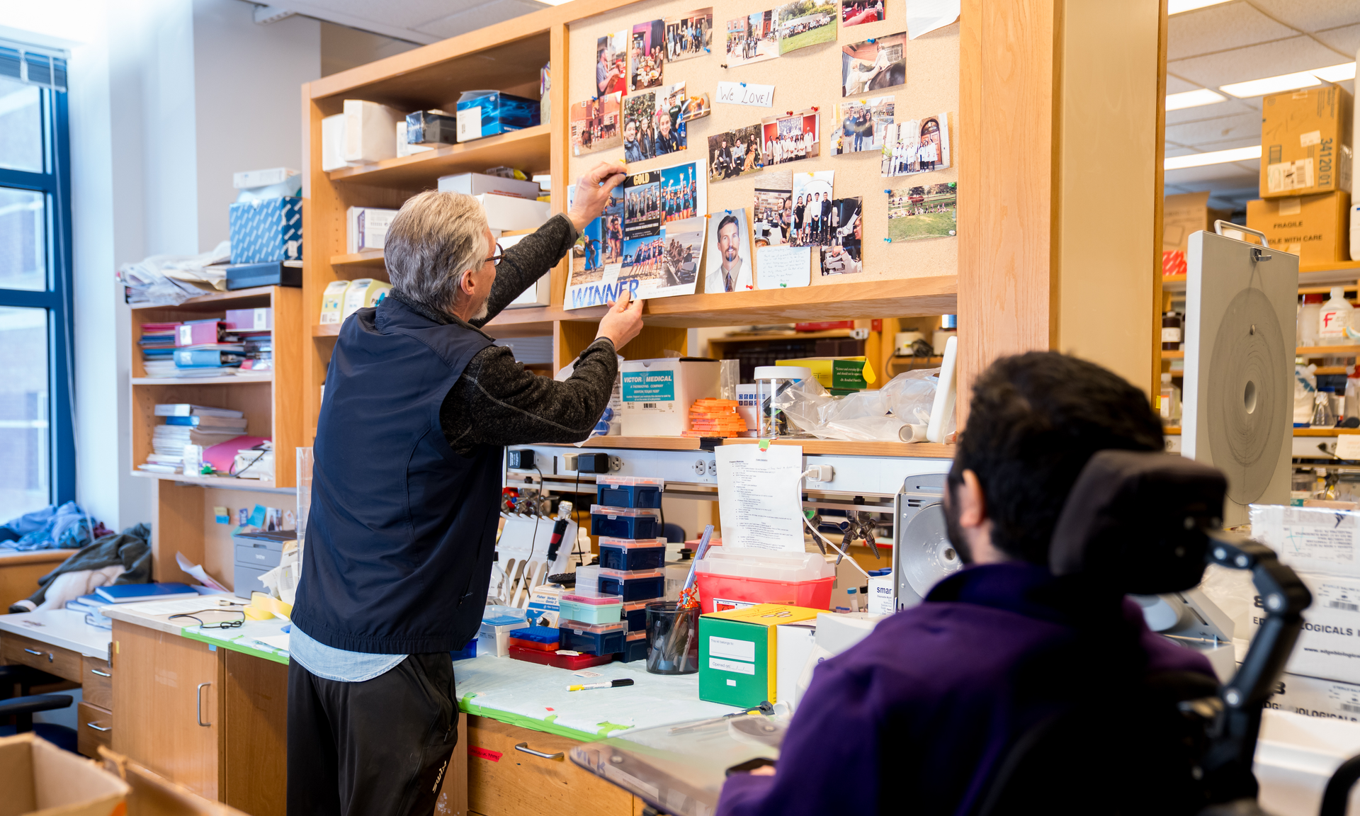Hansell Stedman reaches to unpin a poster from a bulletin board celebrating Coral Kasden’s rowing win, while Yuva Gambhir watches