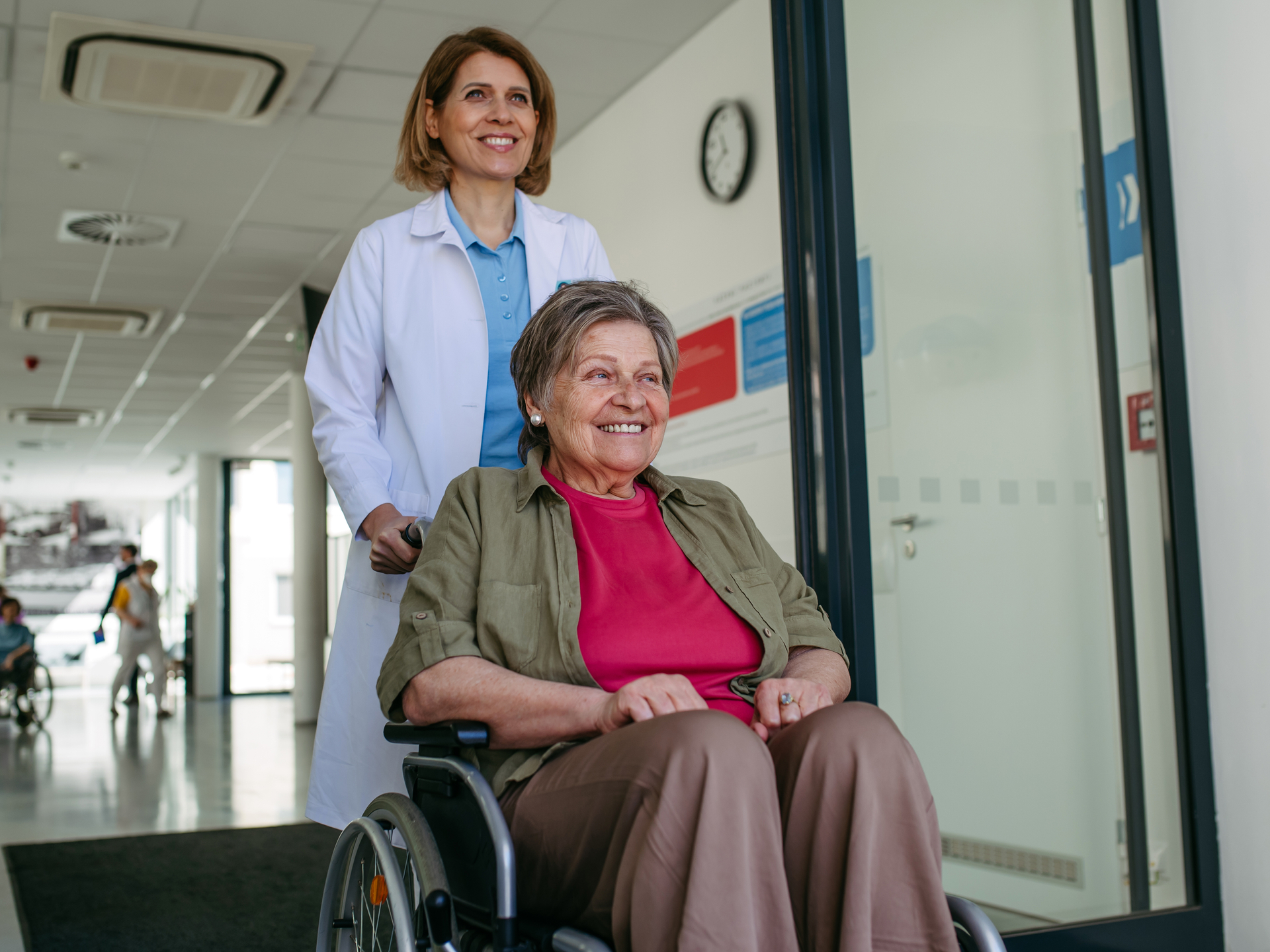Doctor pushing a patient in a wheelchair down a hospital hallway.