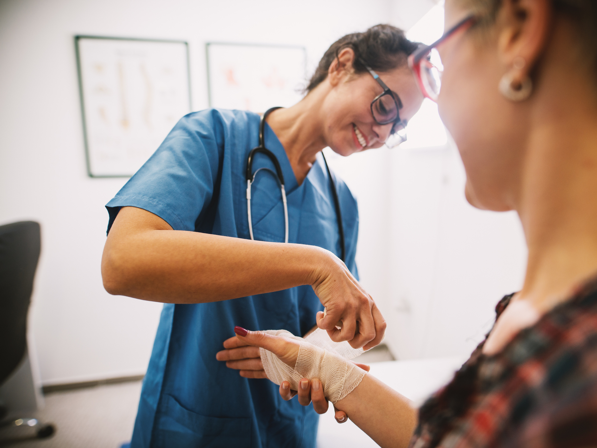 Professional nurse at the hospital bandaging the hand with a medical bandage for a woman patient.