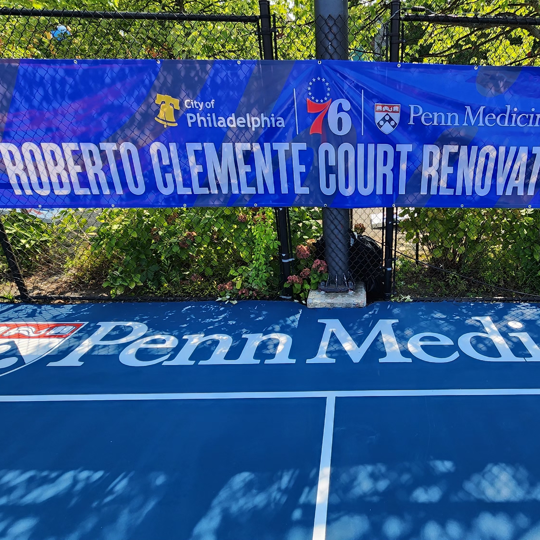 A banner on a fence reads: Roberto Clemente Court Renovation Unveil, above the Penn Medicine logo on the court itself