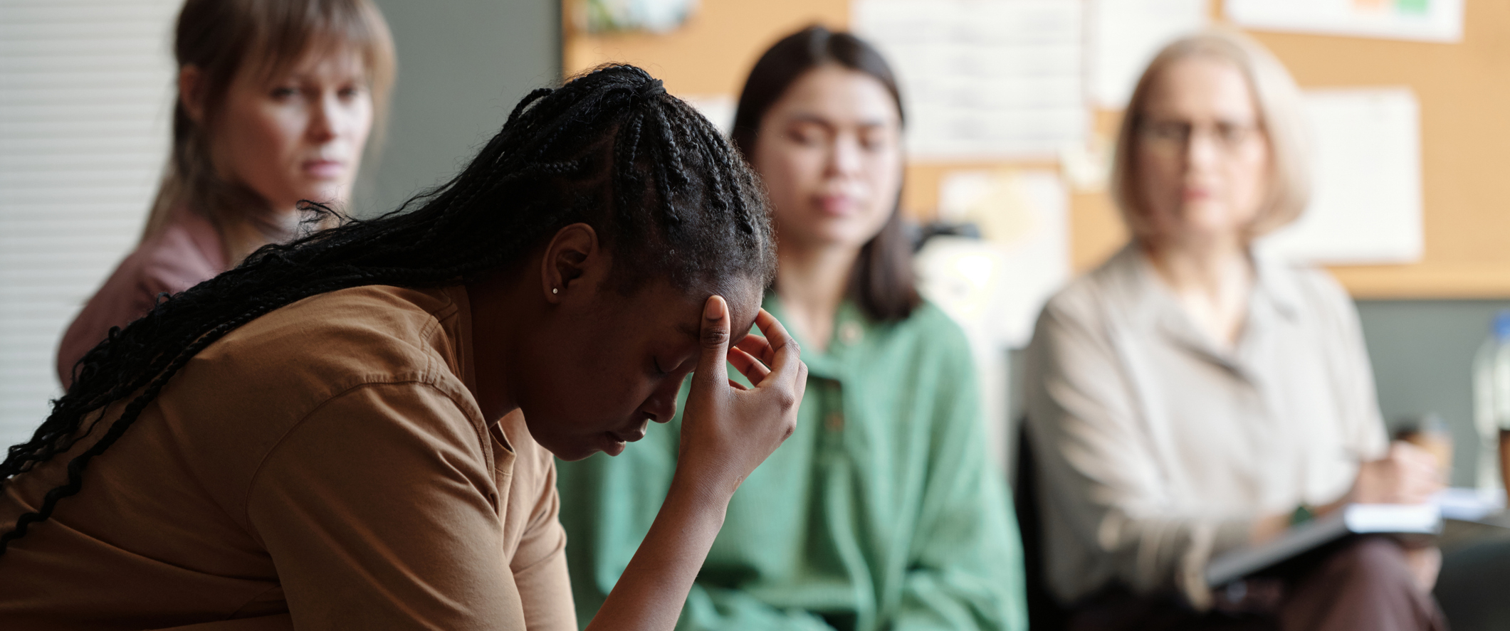 A woman in a support group, looking down with her hand on her forehead