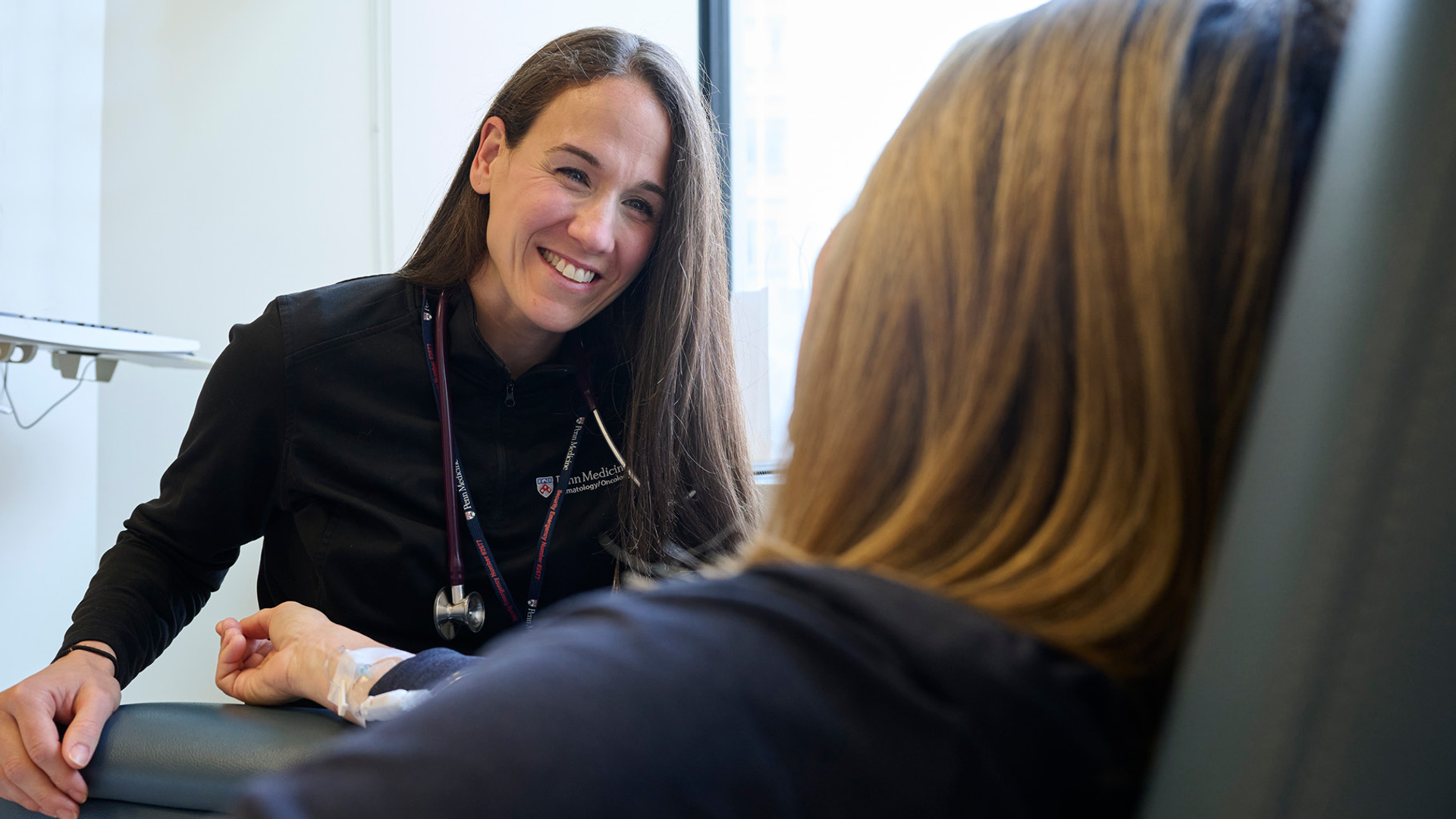 A nurse smiles at a female patient who is seated in an infusion chair