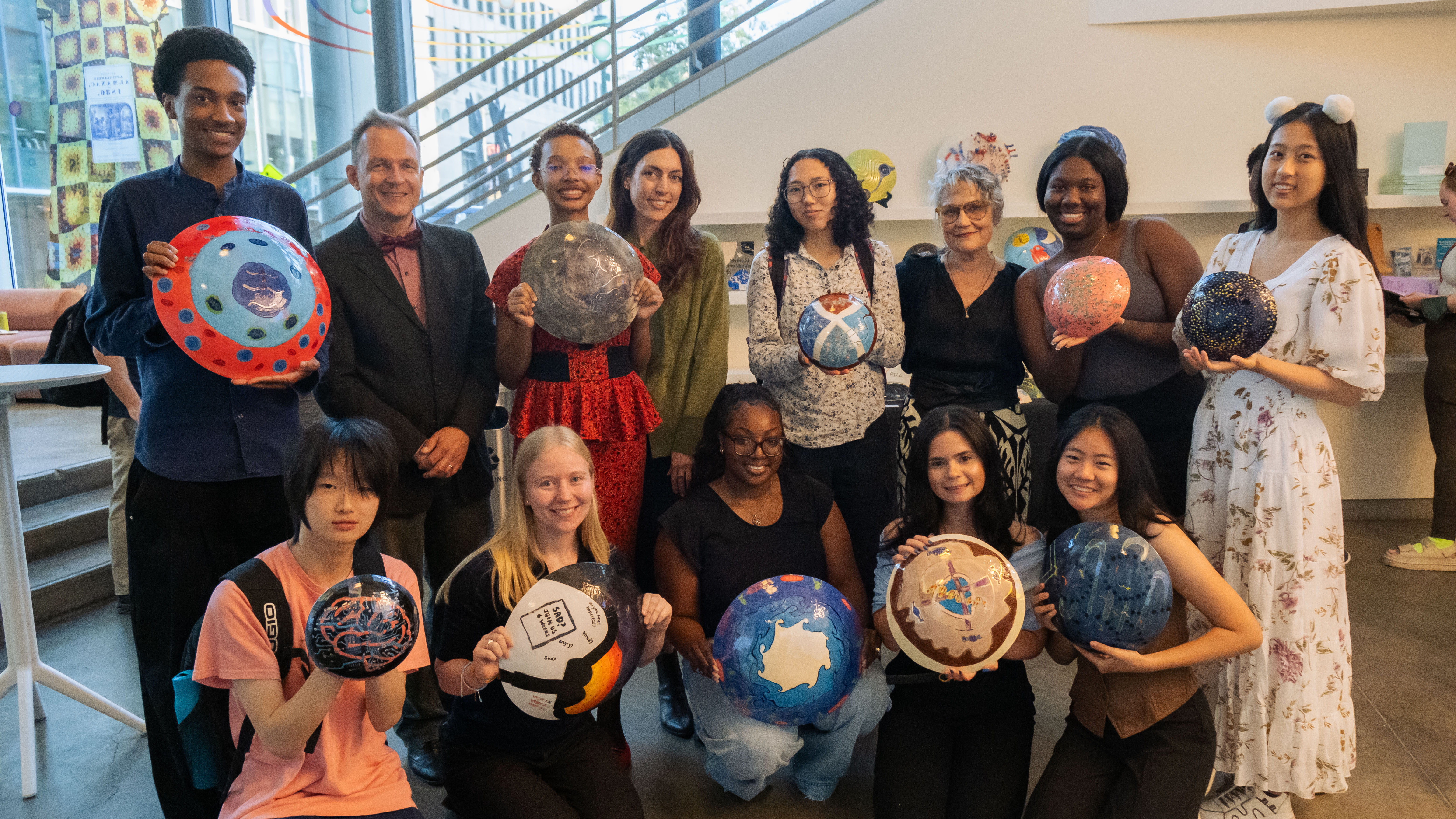 A group shot of students holding ceramic shields, painted with artwork.