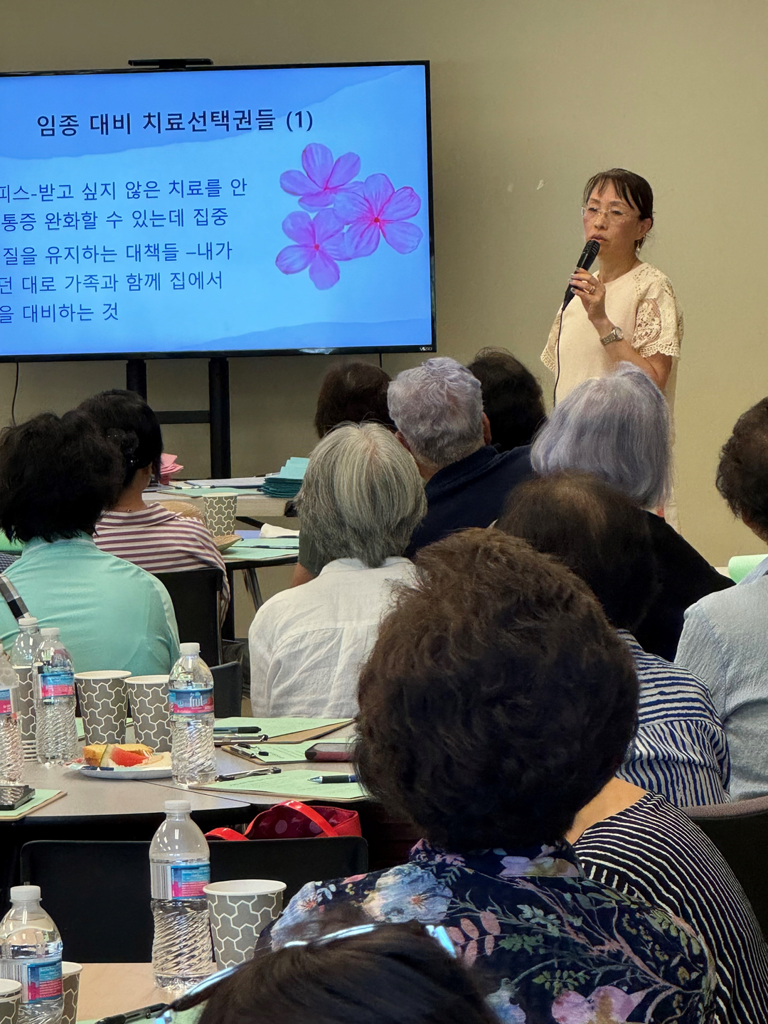 Eunice Park-Clinton stands in front of a room of seniors, speaking with a microphone