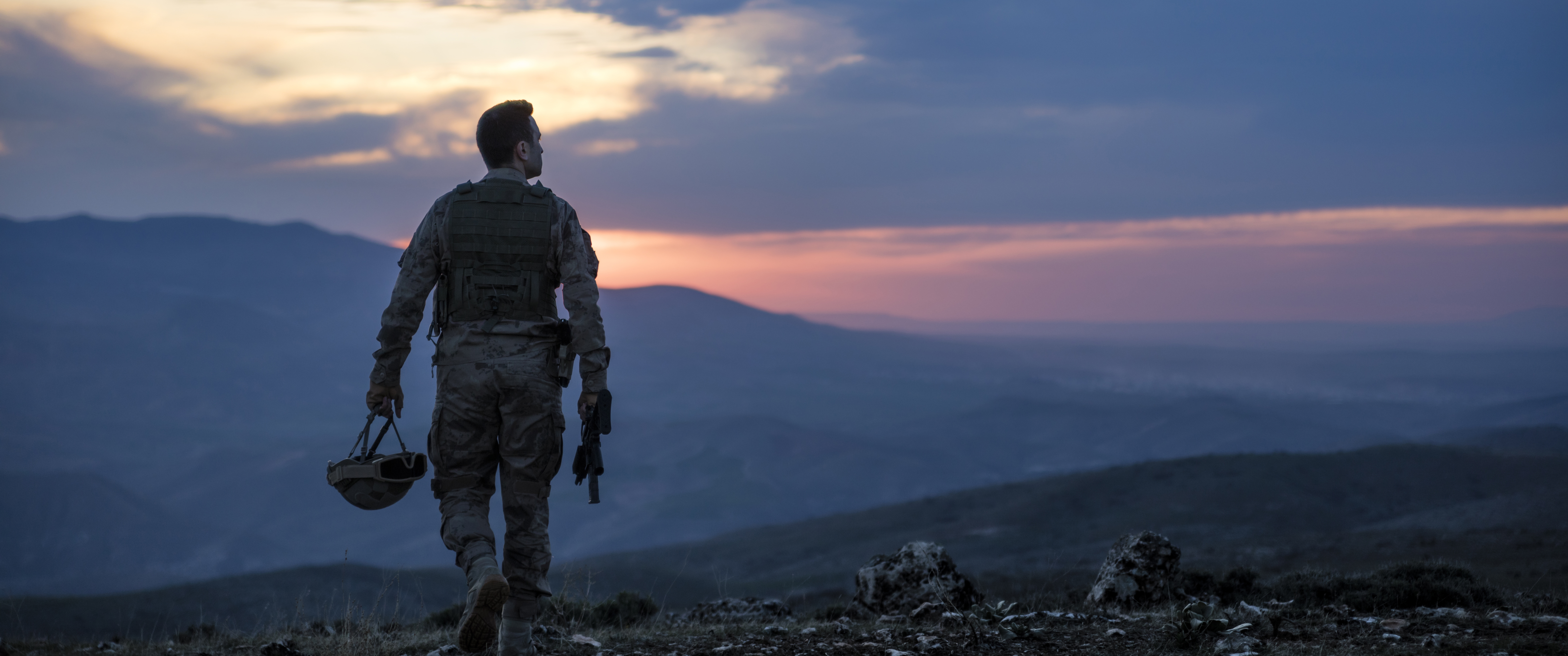 Military soldier walking on a mountain at sunset