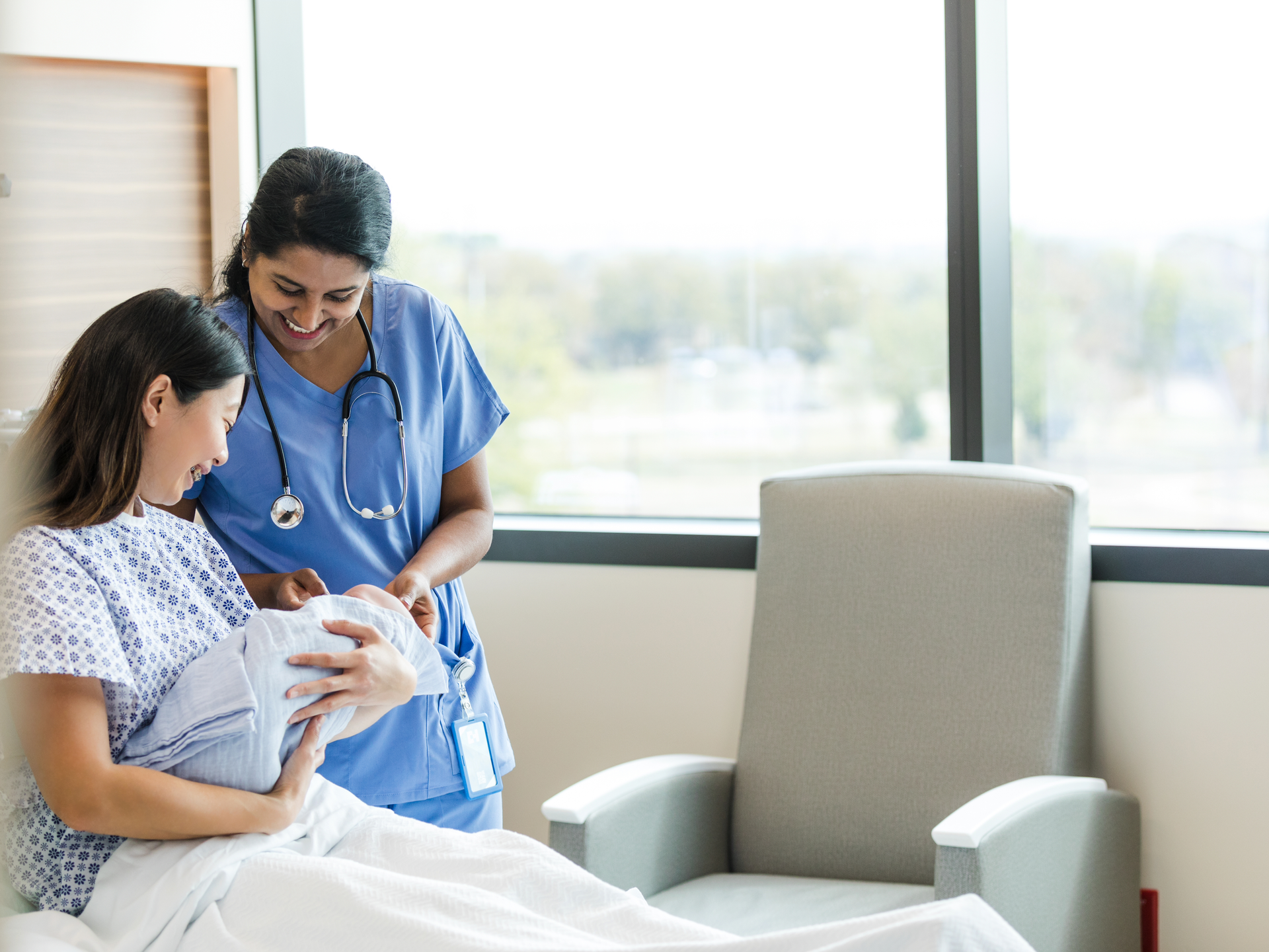 Nurse smiles and admires the baby with the new mother