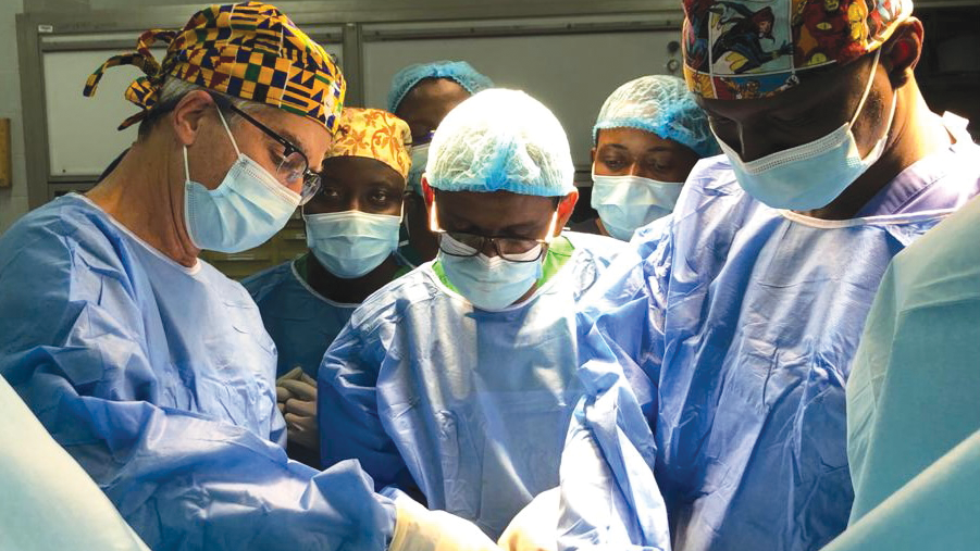 Albert Ruenes performing surgery and teaching medical professionals in an operating room wearing surgical gowns, masks, and caps.