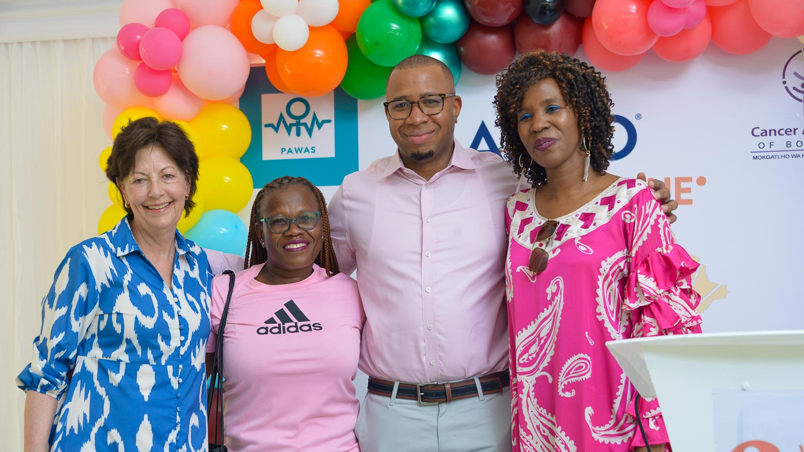 Lynn Schuchter, Mogametsi Setswamorago, Farouk Dako, and Miriam Mutebi in front of a banner with colorful balloons