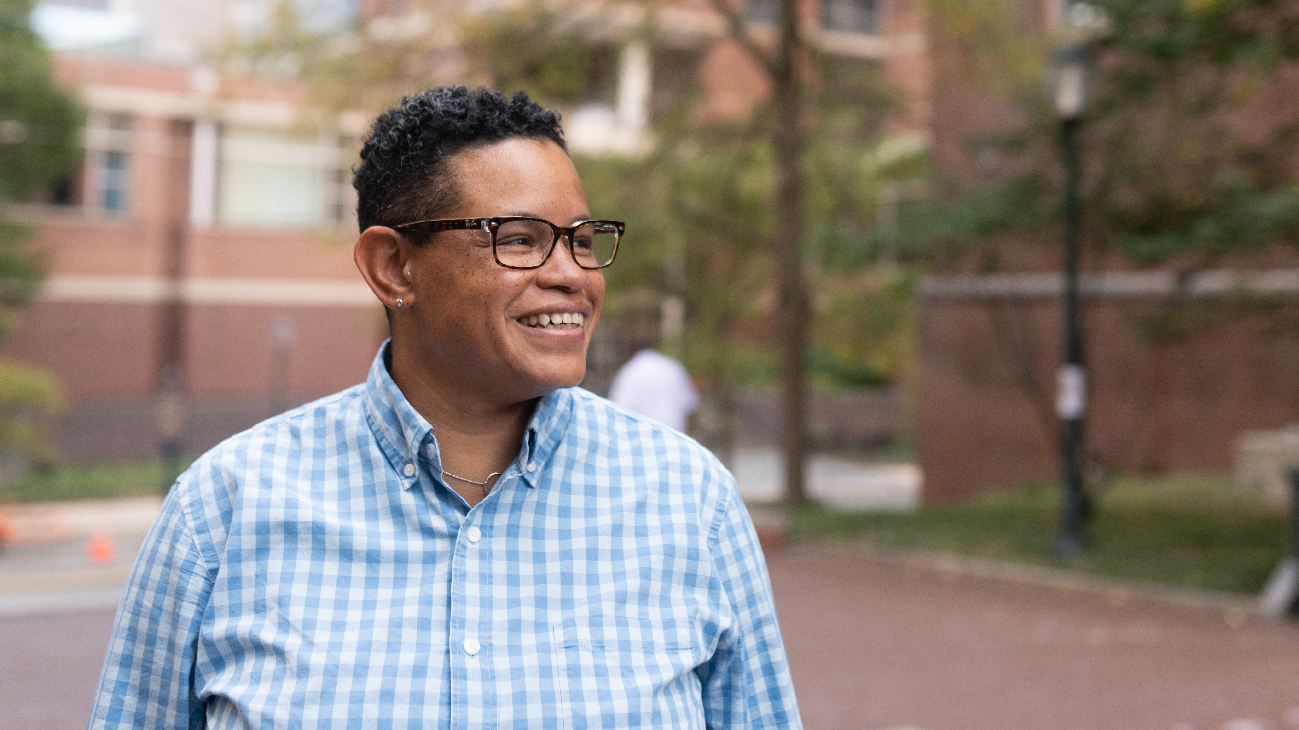 Donita Brady smiling on a campus with buildings and a tree-lined path in the background.