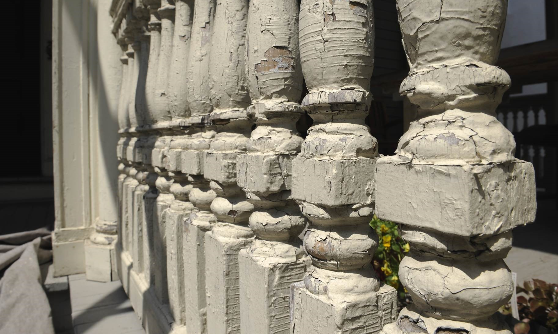 Close-up of a porch railing with lead painting on wooden balusters showing cracked and peeling paint, viewed at an angle.