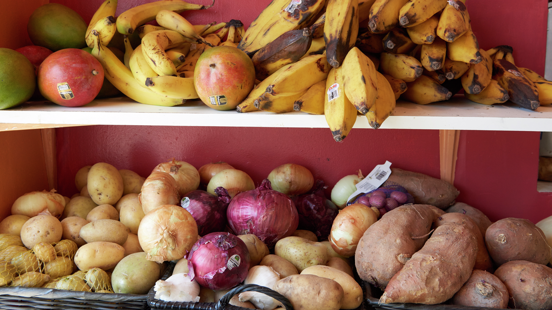 A shelf filled with produce including bananas, onions, and potatoes