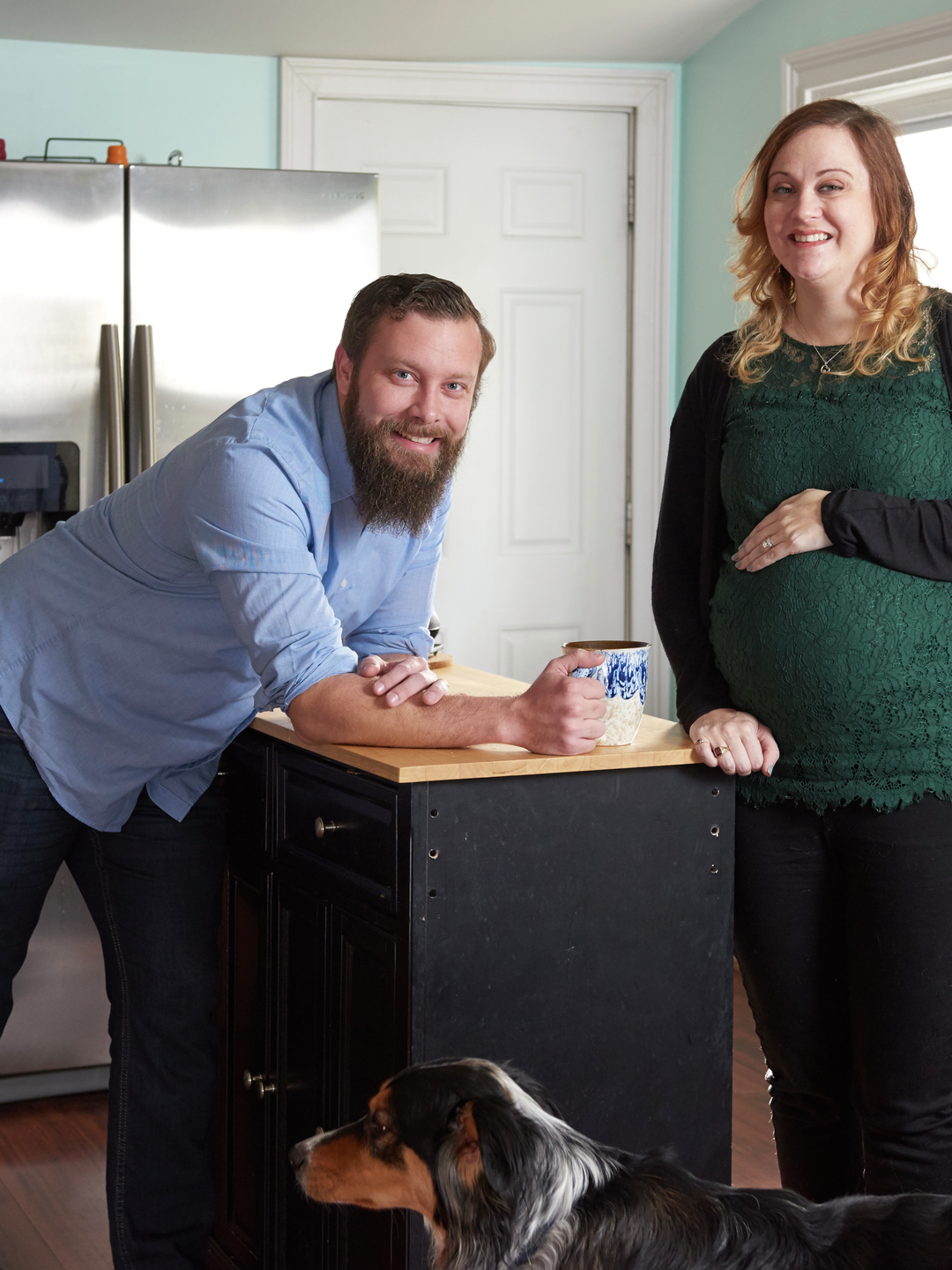 Drew and Jennifer Gobrecht at their kitchen island, Jennifer holding her hand over her pregnant belly