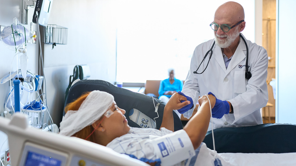 A patient in a hospital bed grips a doctor’s hands as part of a neurology exam