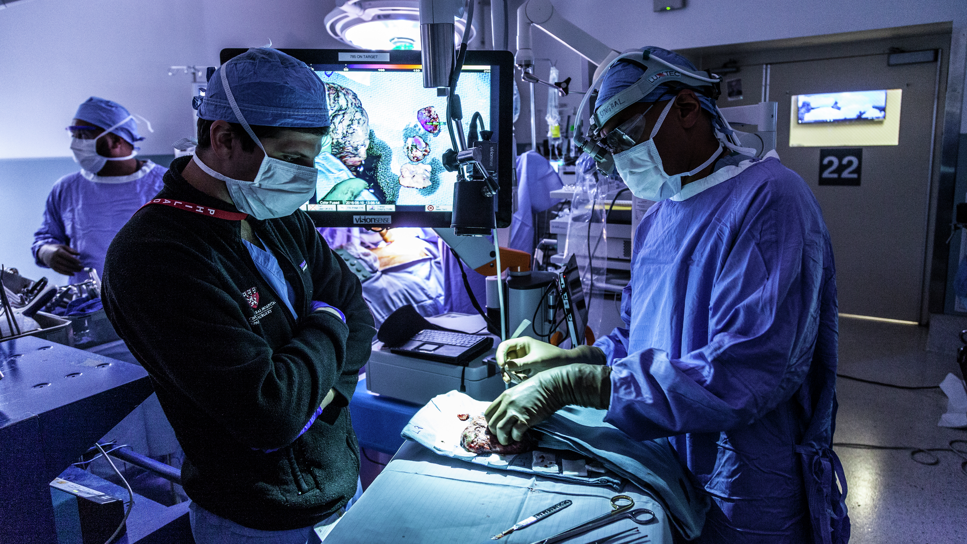 Alongside other personnel in an operating room, Sunil Singhal examines lung tissue treated with a glowing tumor compound