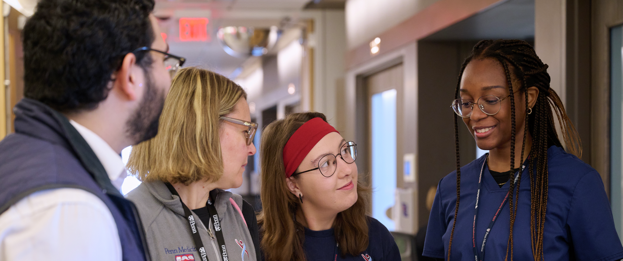 Four Clinical Research staff members have a conversation around a cart in a hospital hallway