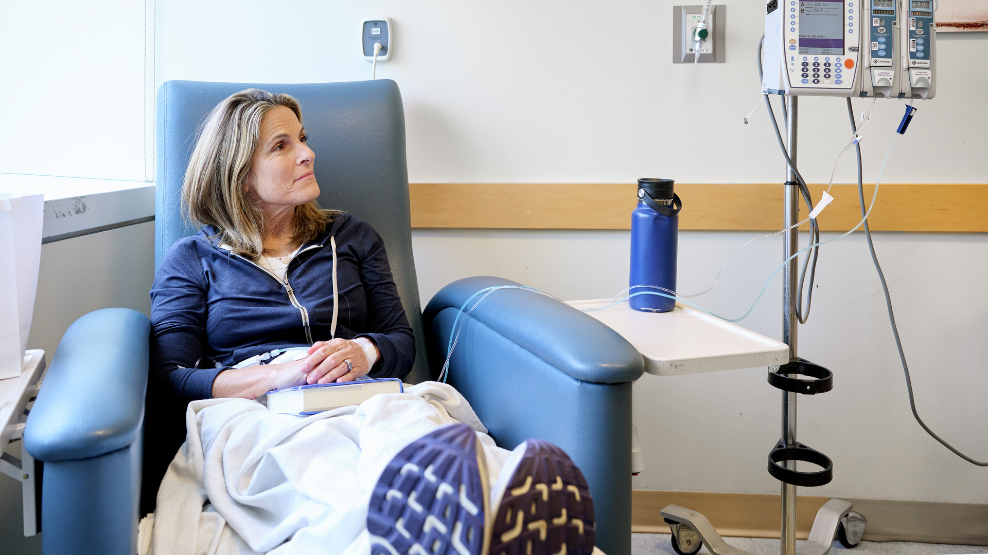 Amy Darragh, seated in an infusion chair receiving chemotherapy, looks up and to the right with a peaceful, optimistic expression