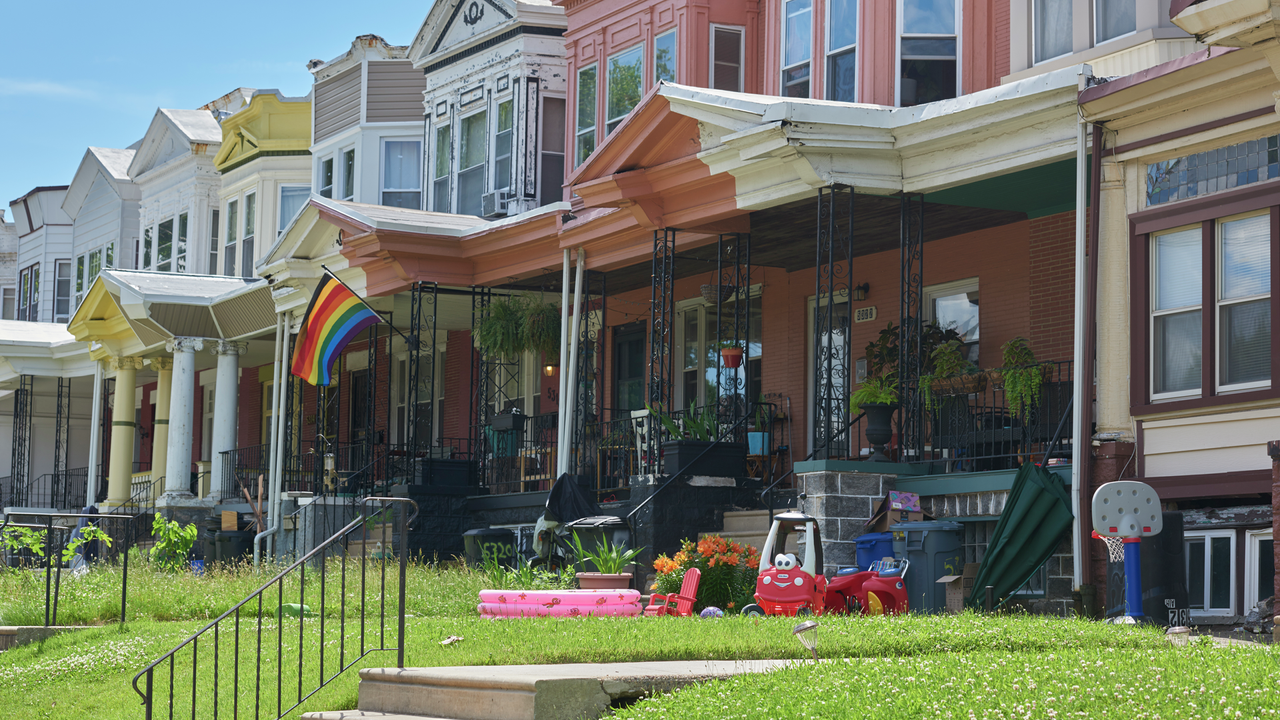 Row houses in Philadelphia of various colors, one with a Pride flag and one with children's toys on the front porch and lawn