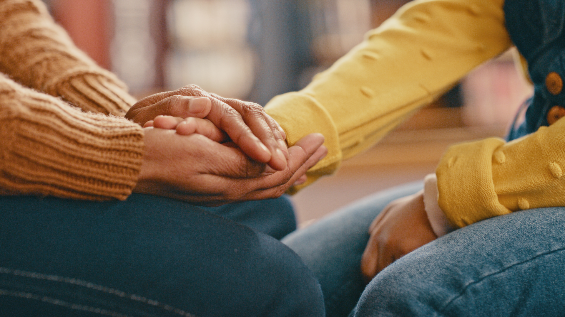 A woman sitting down holding another woman's hand, suggesting she is providing emotional support