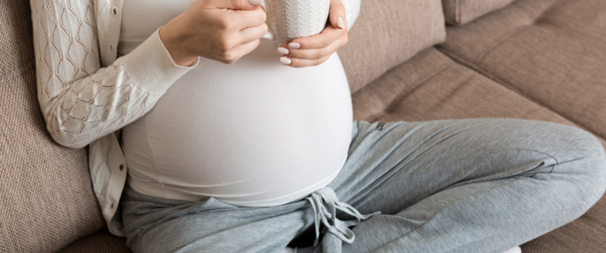 A pregnant person sitting on a couch holding a cup of coffee