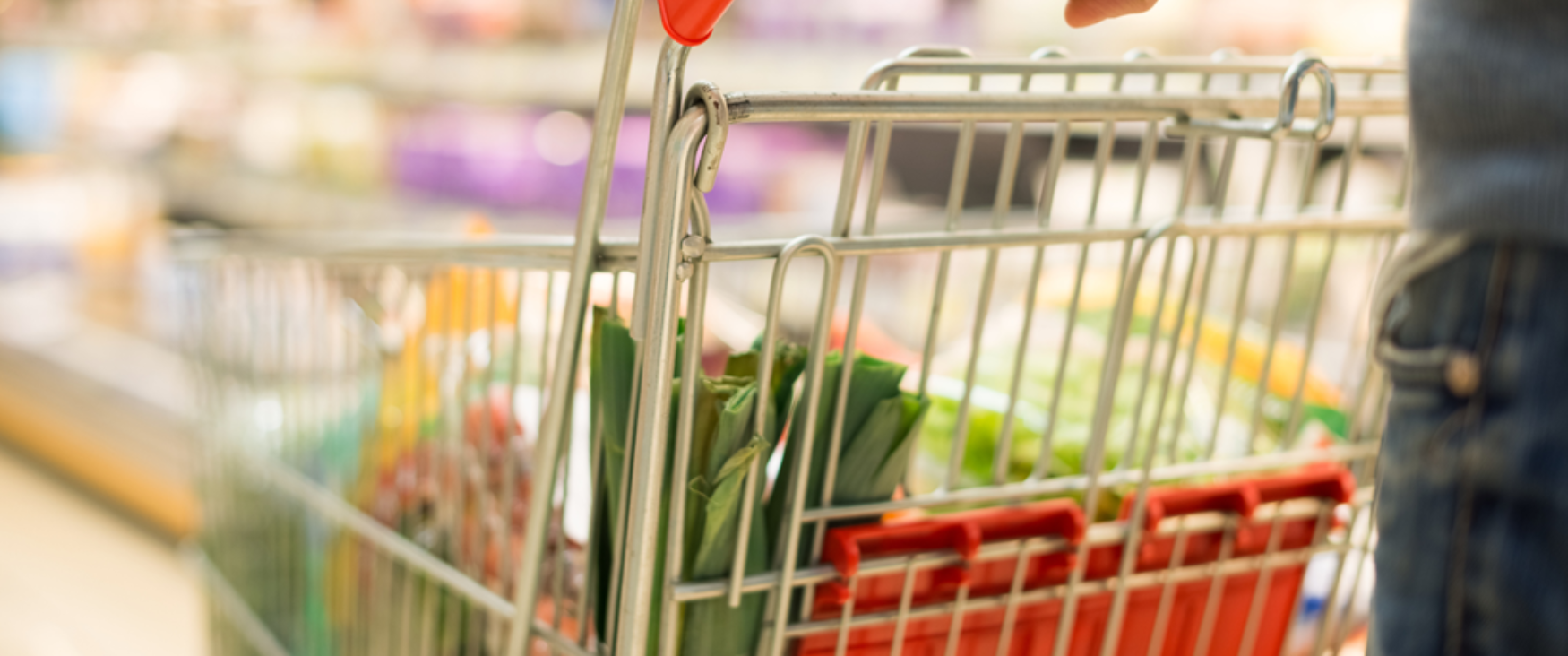 A grocery cart being pushed down the aisle in a store, filled with food