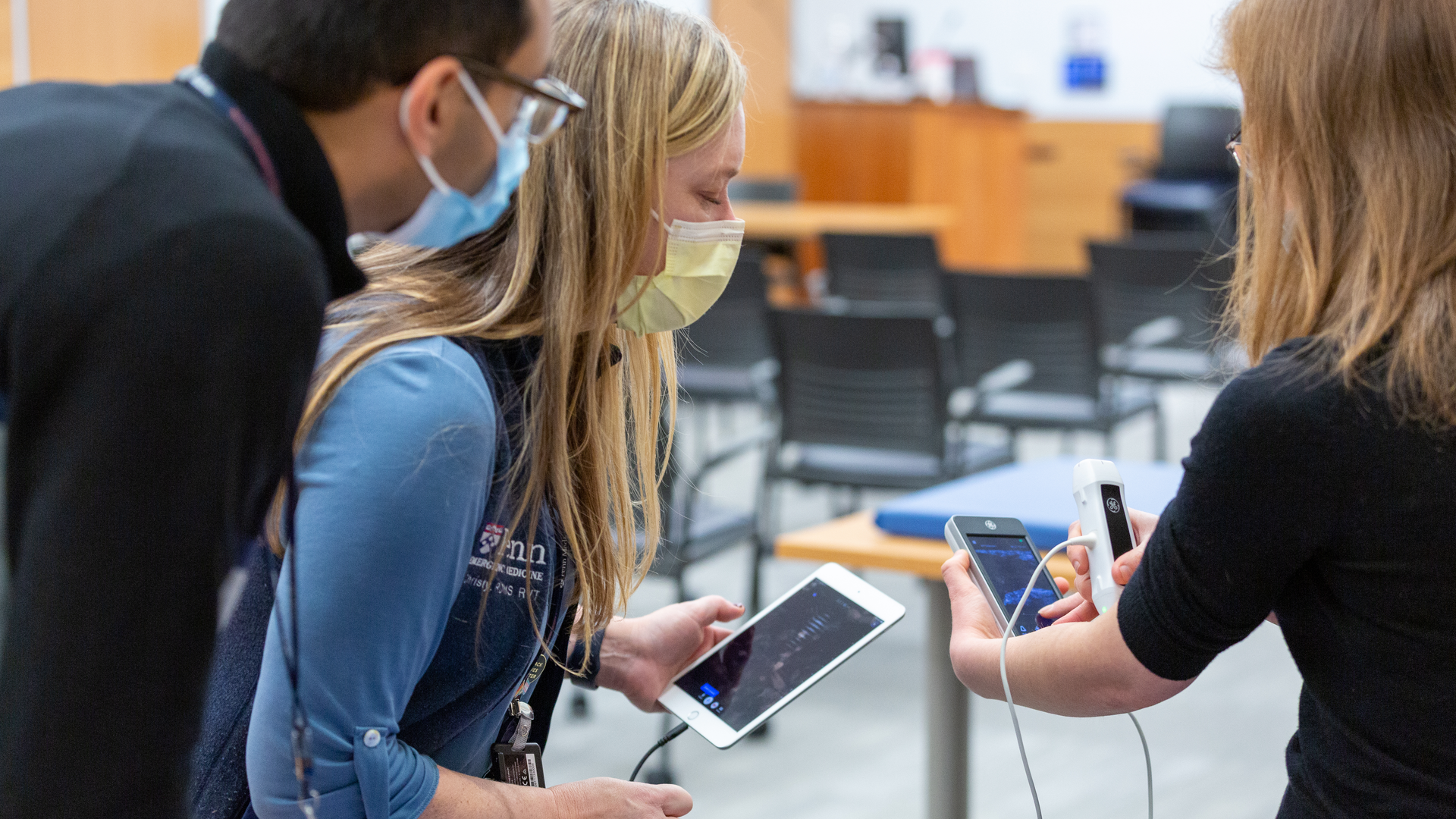 Christy Moore looks at a tablet screen as a male faculty member looks over her shoulder and medical student Taylor Daniel points