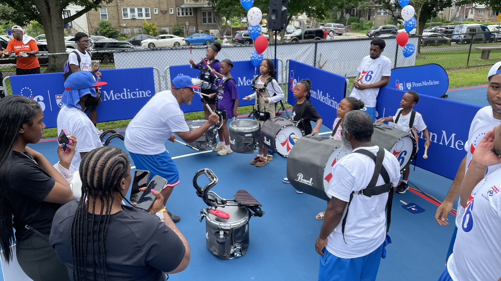 A man instructing a group of children how to play the drums on a basketball court