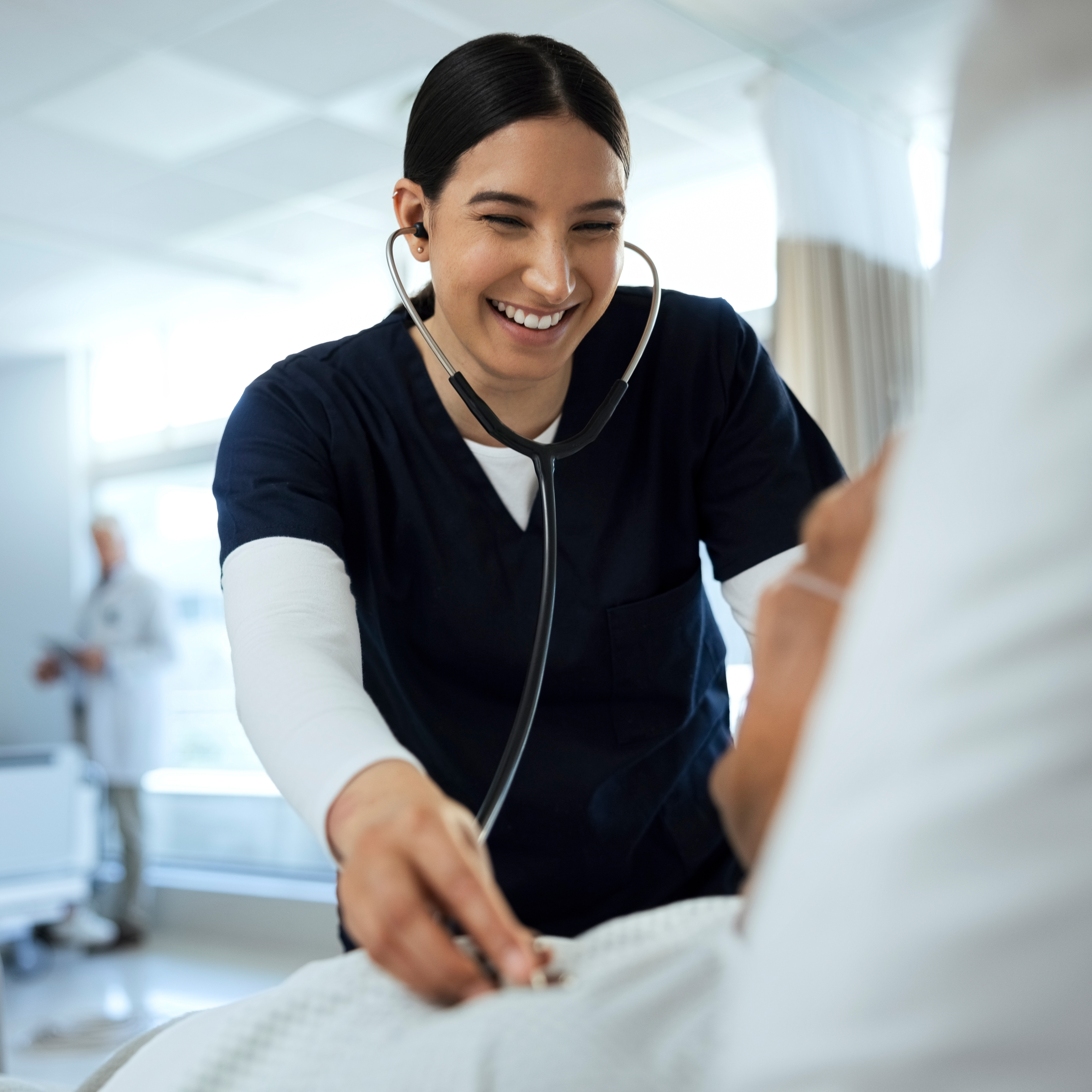 Happy woman, caregiver and listening to patient heart rate, beat or monitoring for healthcare checkup on bed at hospital