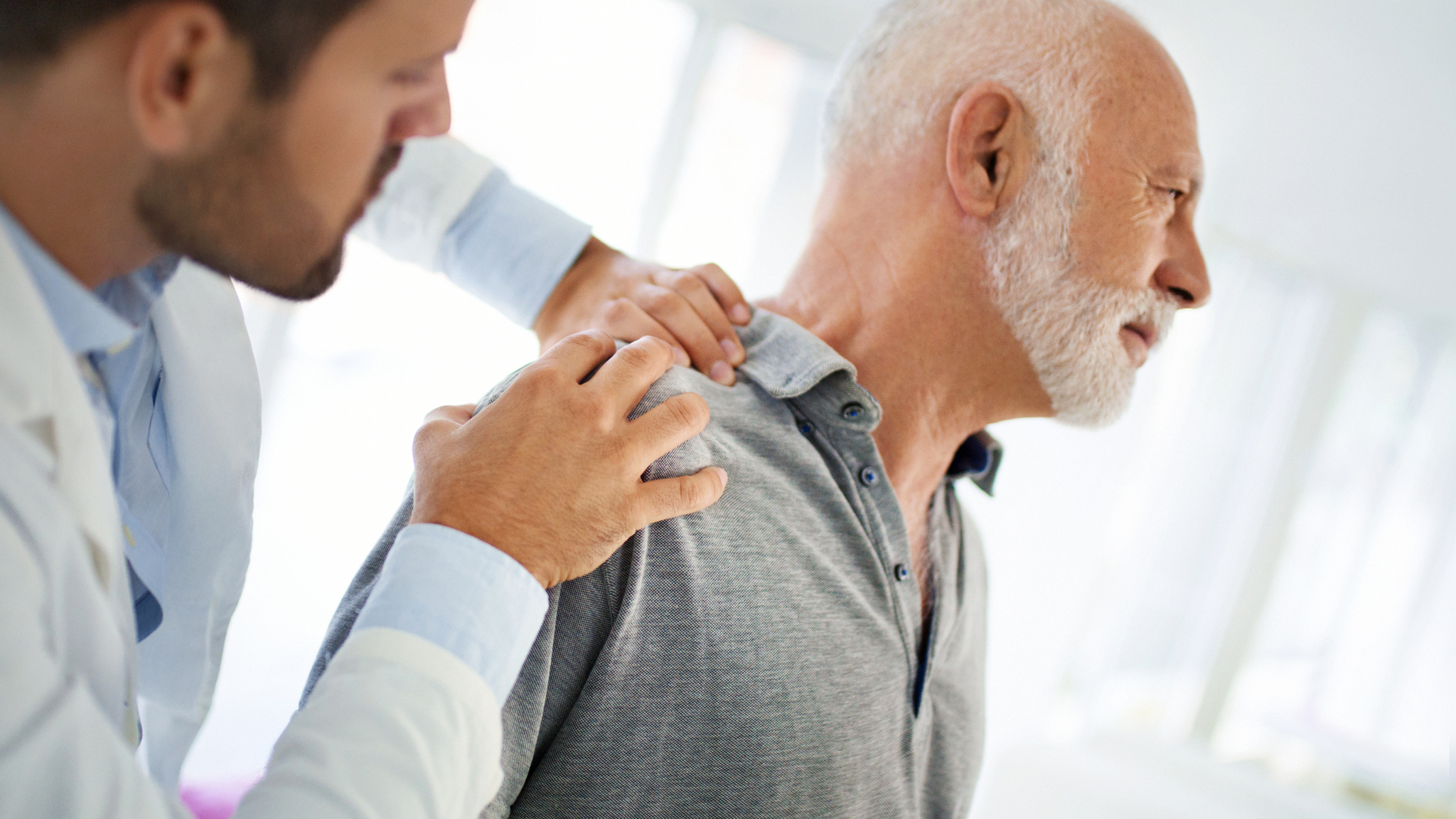 The doctor is touching the sensitive area of a patinet shoulder and trying to determine the cause of pain.