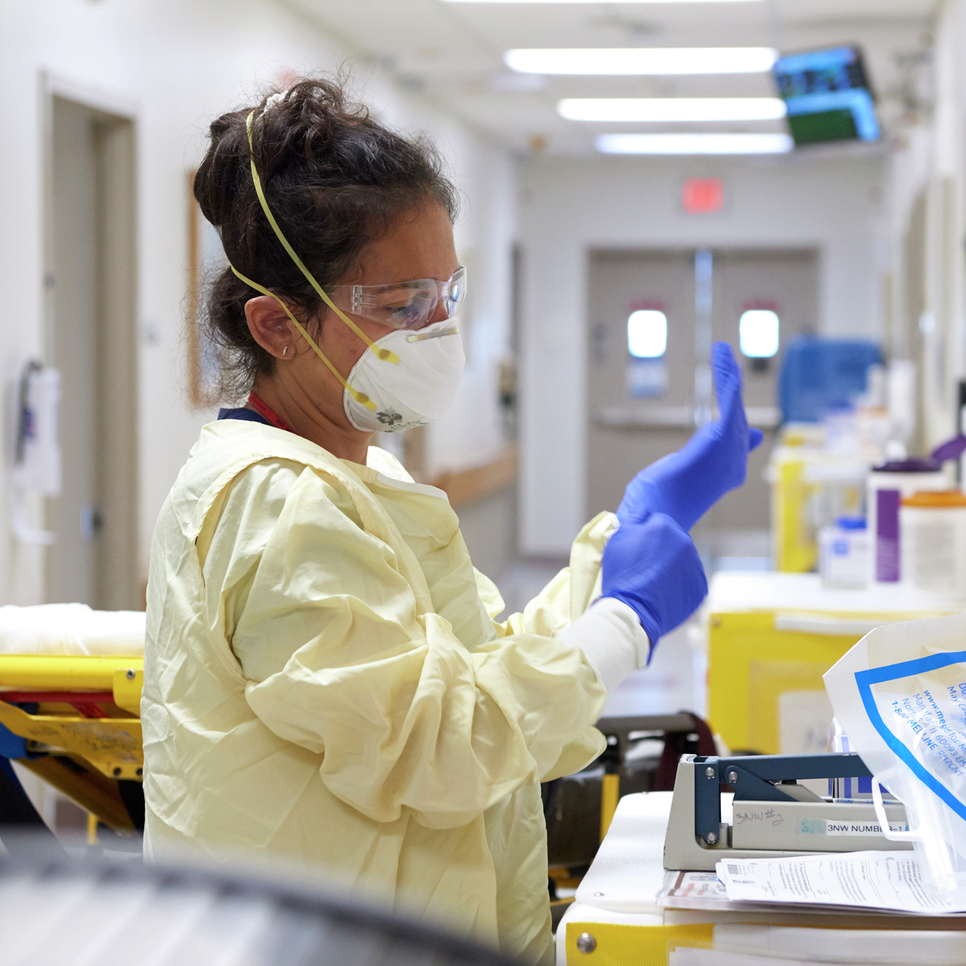 A clinician in a hallway dons gloves with a gown