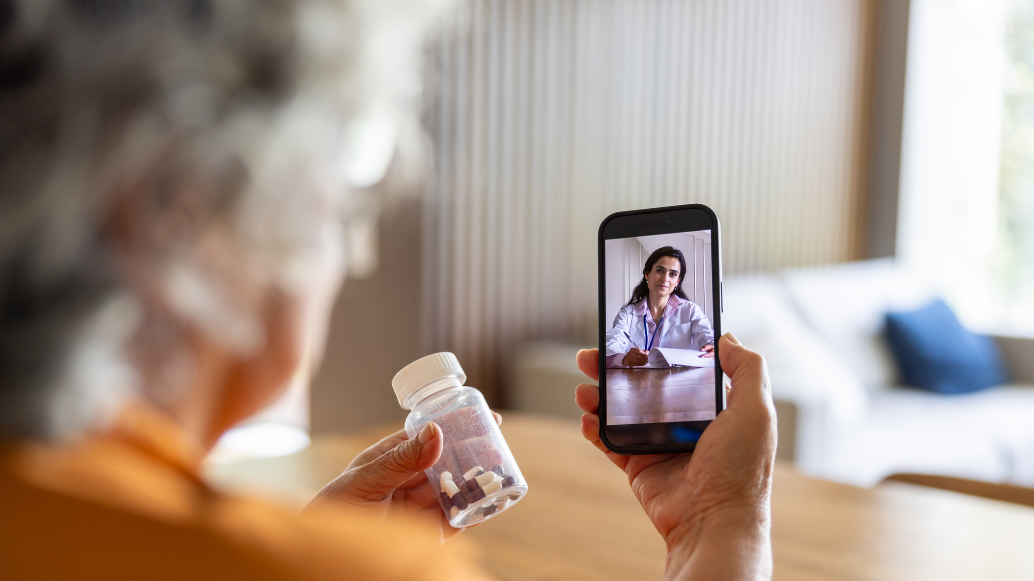 A woman talking to a doctor on a phone while holding pill bottle