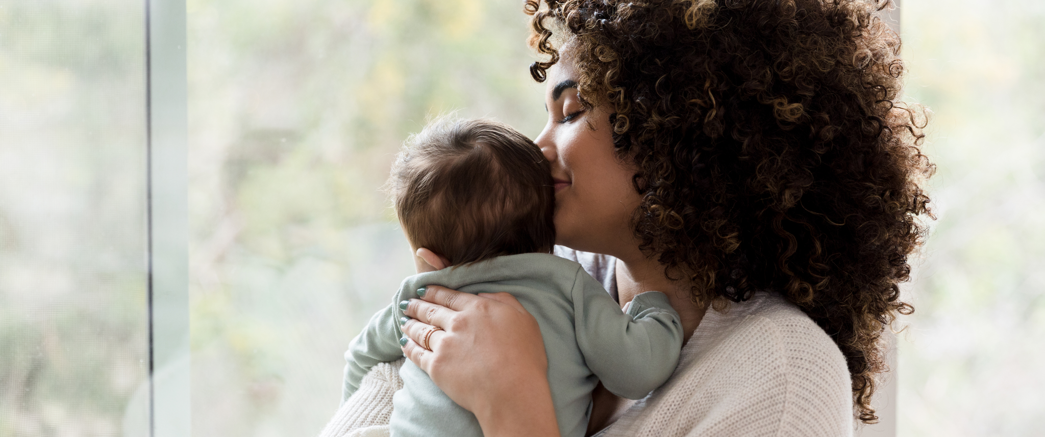 Smiling mother holding infant in front of window, infant facing away
