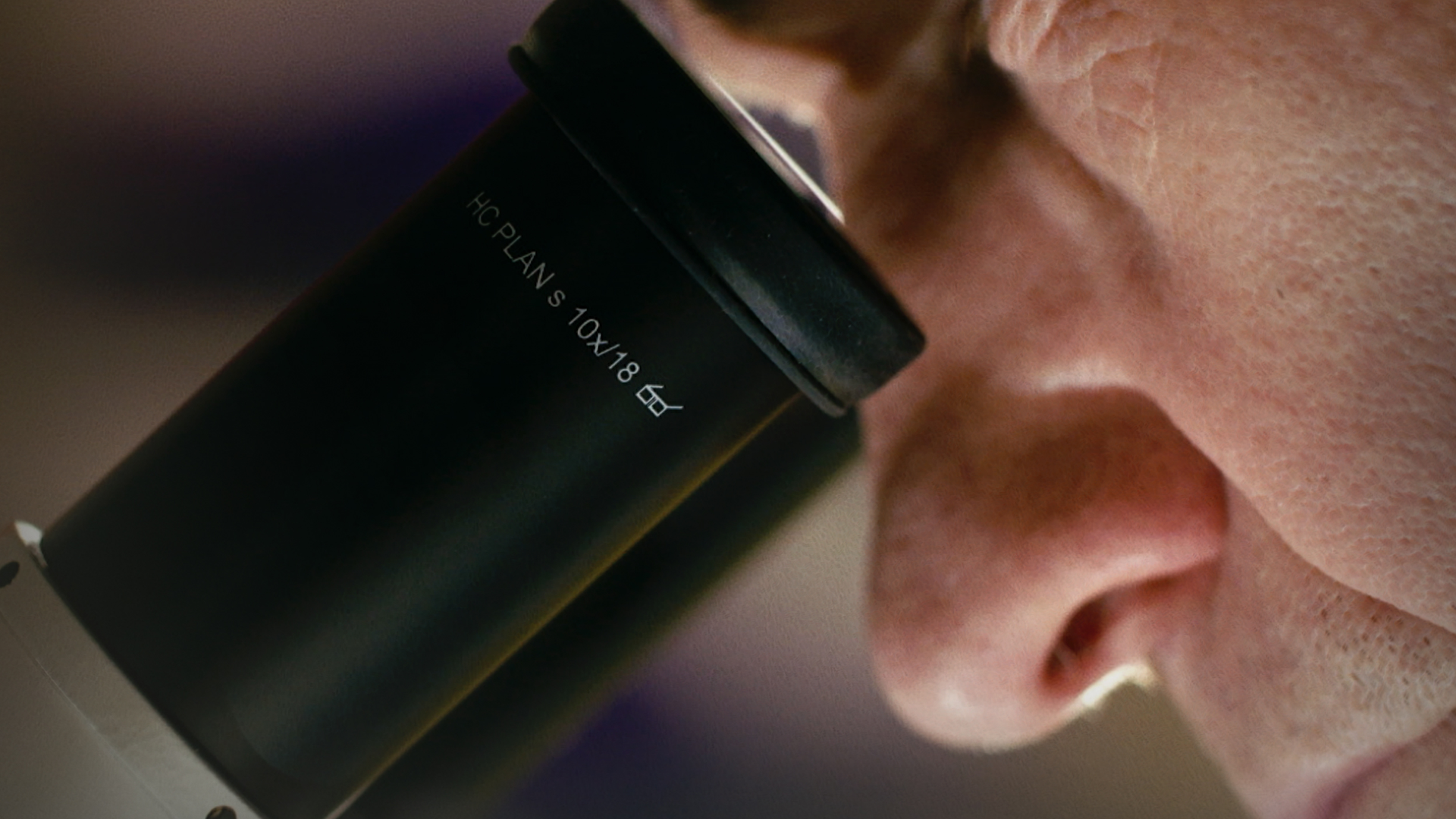 The movie poster of the documentary Of Medicine and Miracles with a close up shot of Carl June looking into a microscope