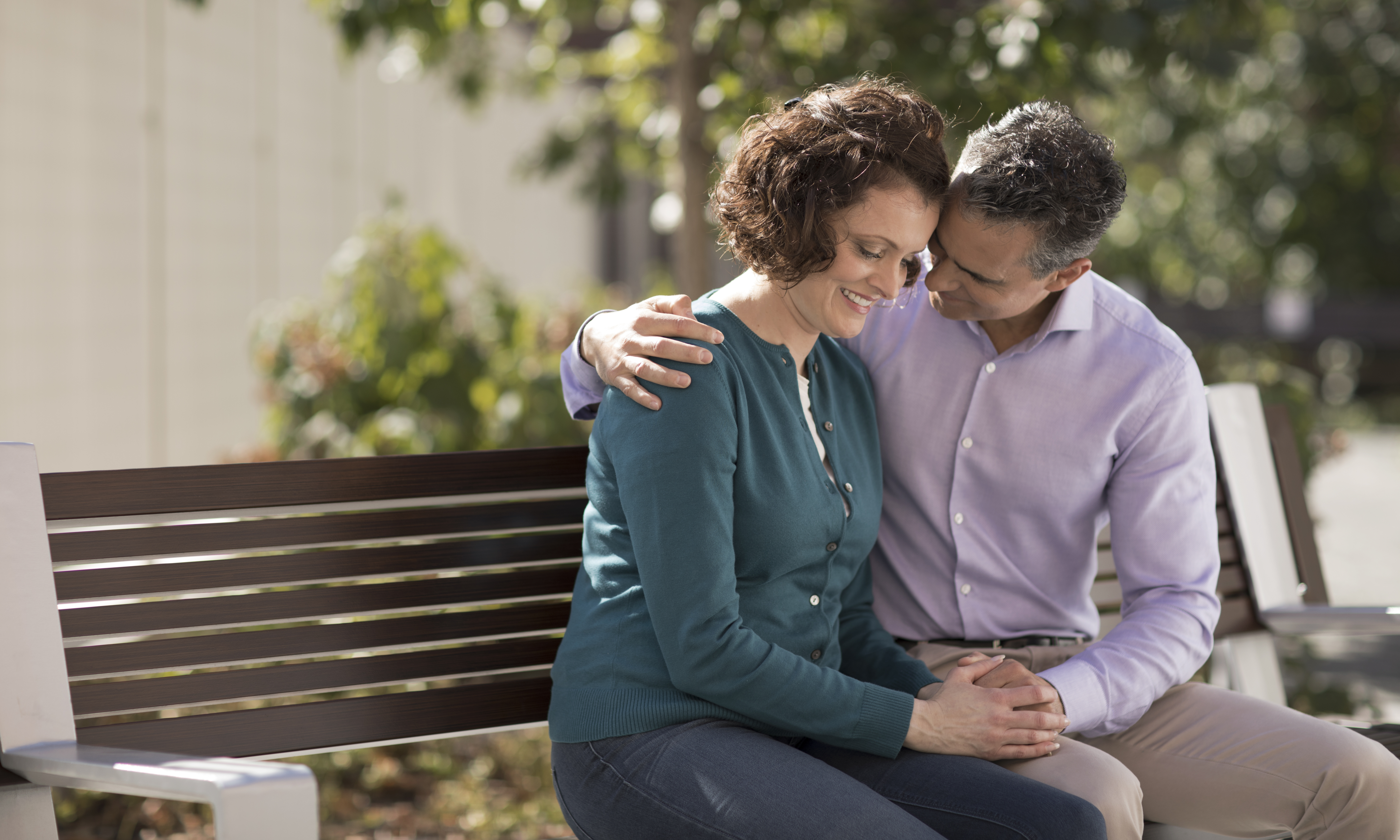 A cancer patient and their spouse embrace happily on bench