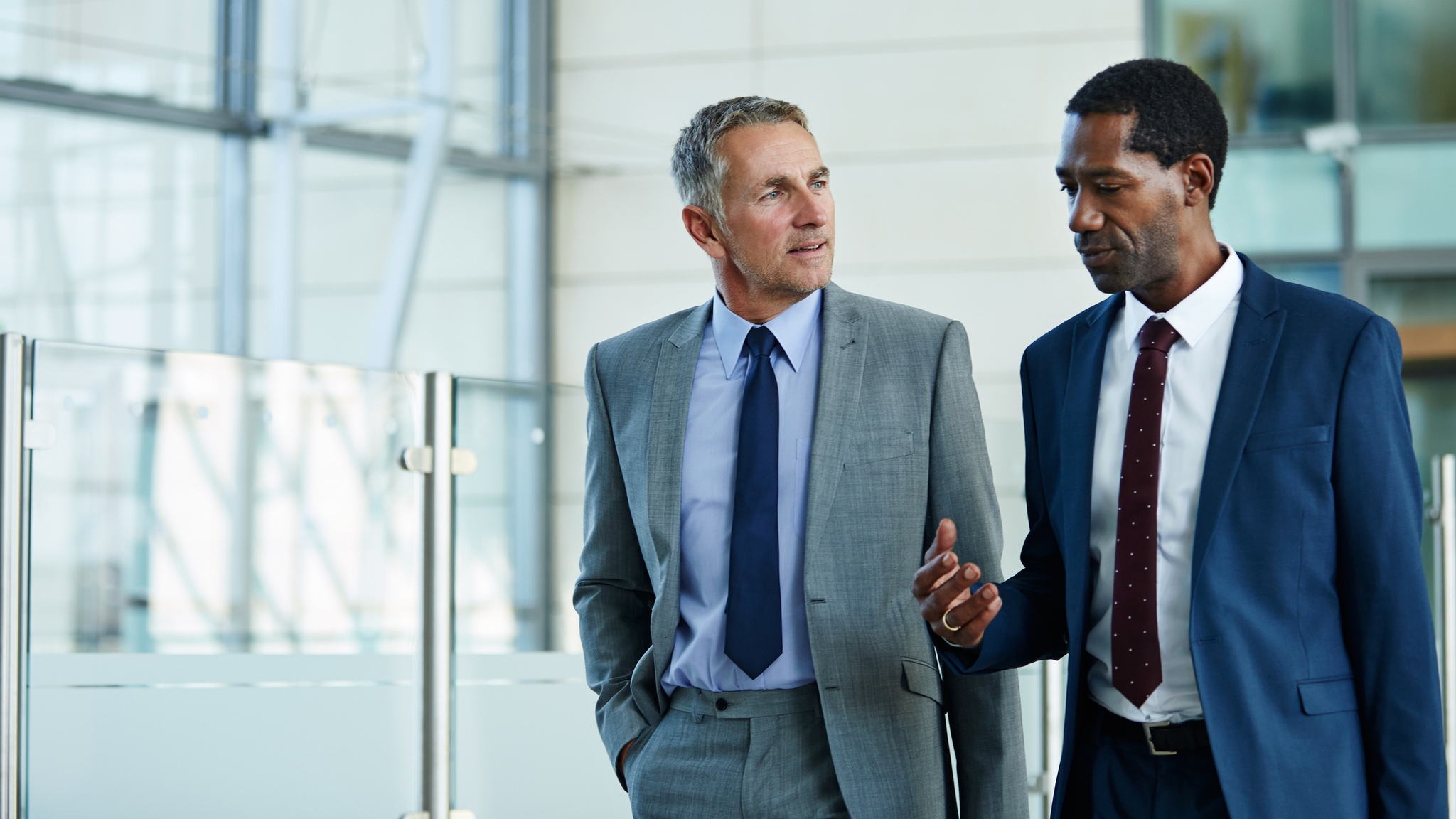 Shot of two businessmen walking and talking together in the lobby of an office building.