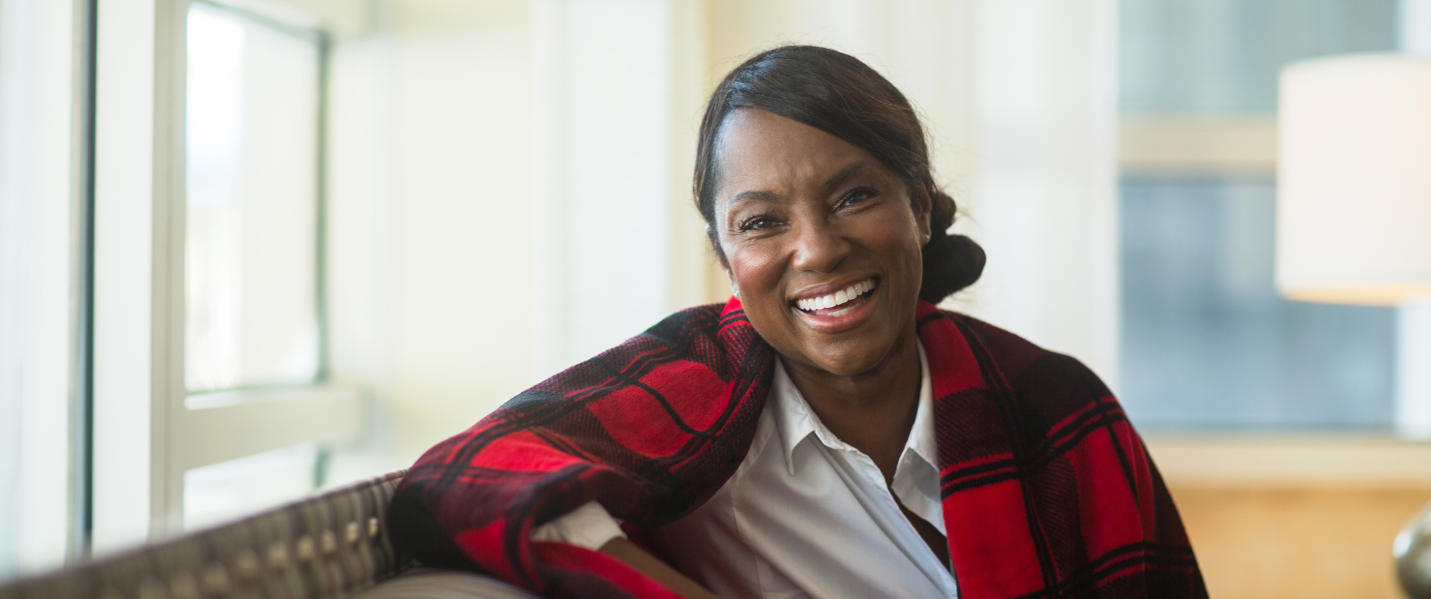 Middle-aged Black woman smiling broadly, sitting on leather couch