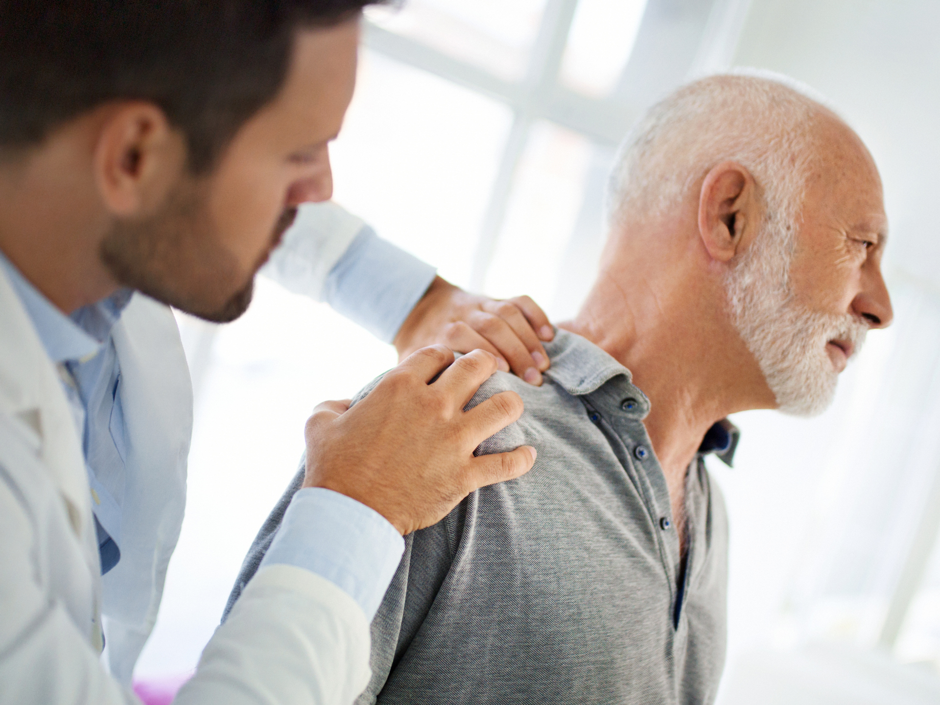 The doctor is touching the sensitive area of a patient shoulder and trying to determine the cause of pain.