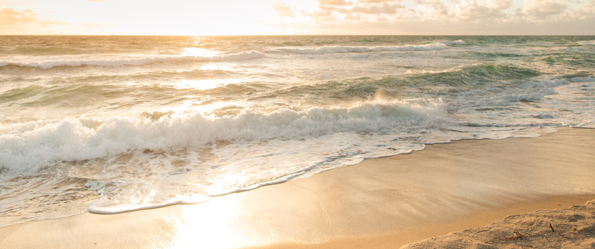 Golden sunrise over beach, with waves crashing on shore