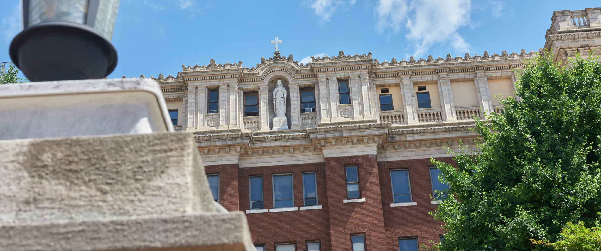 The exterior roofline of the hospital formerly known as Mercy Philadelphia with stone columns, a marble statue, and a cross