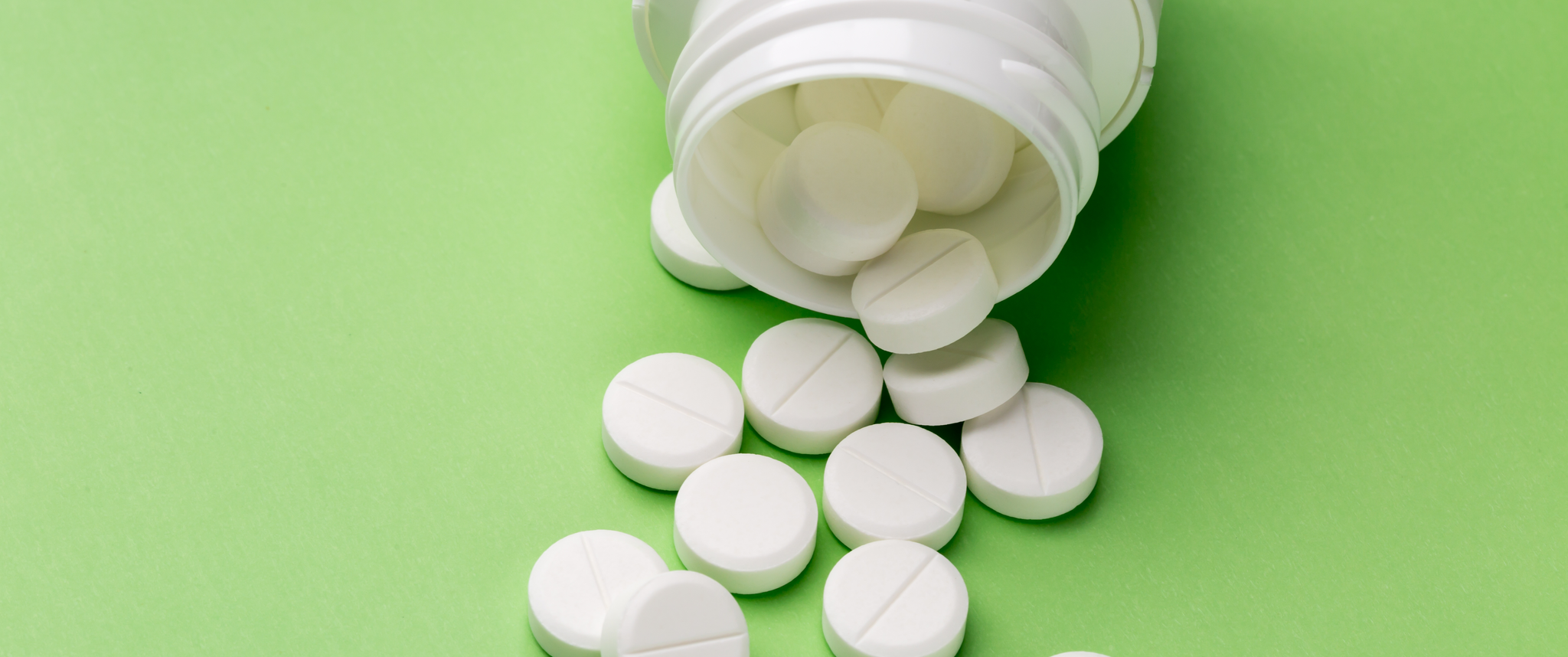 White pills pouring out of a bottle against a green background