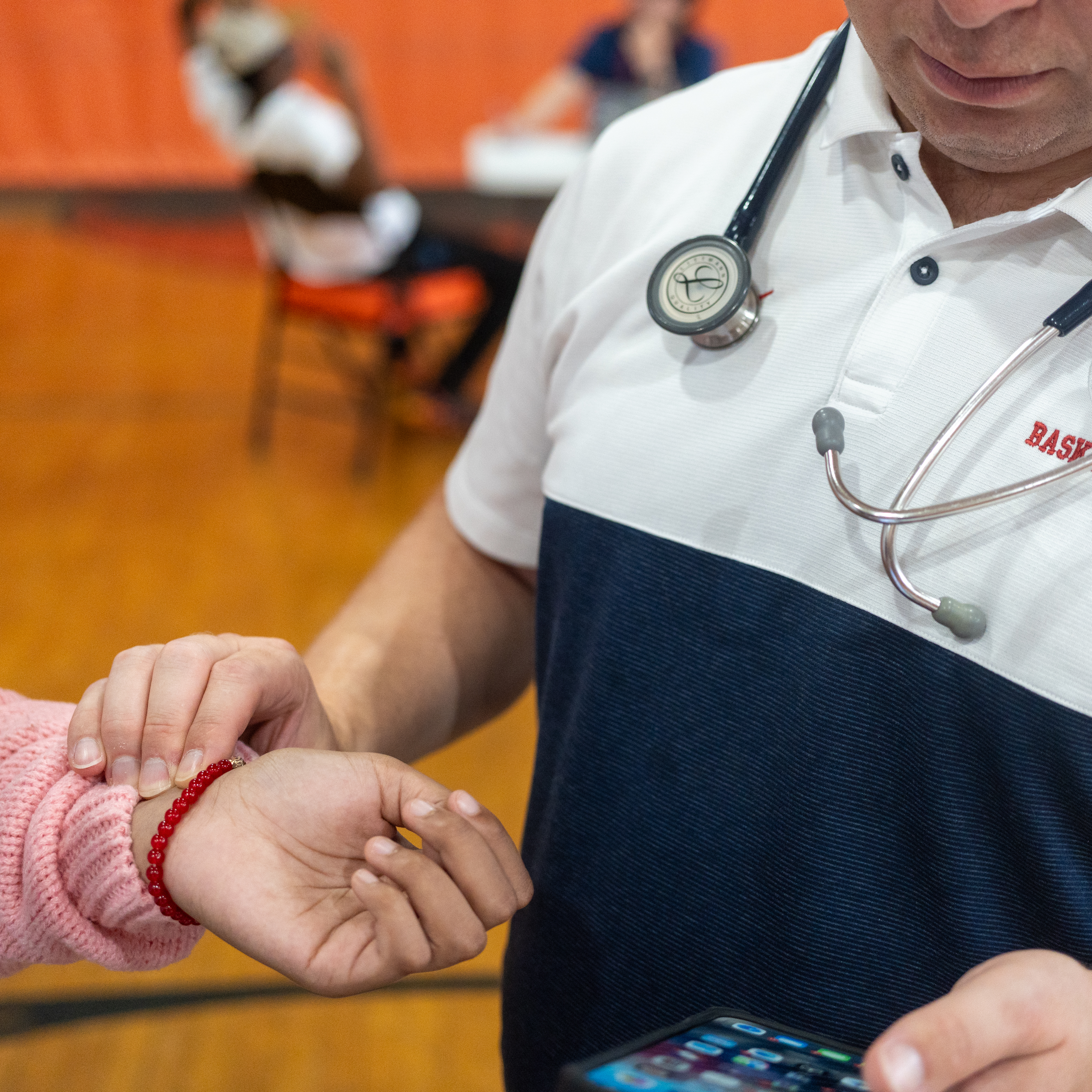 Kris Fayock checking a student's pulse during a sports physical clinic in a school gym