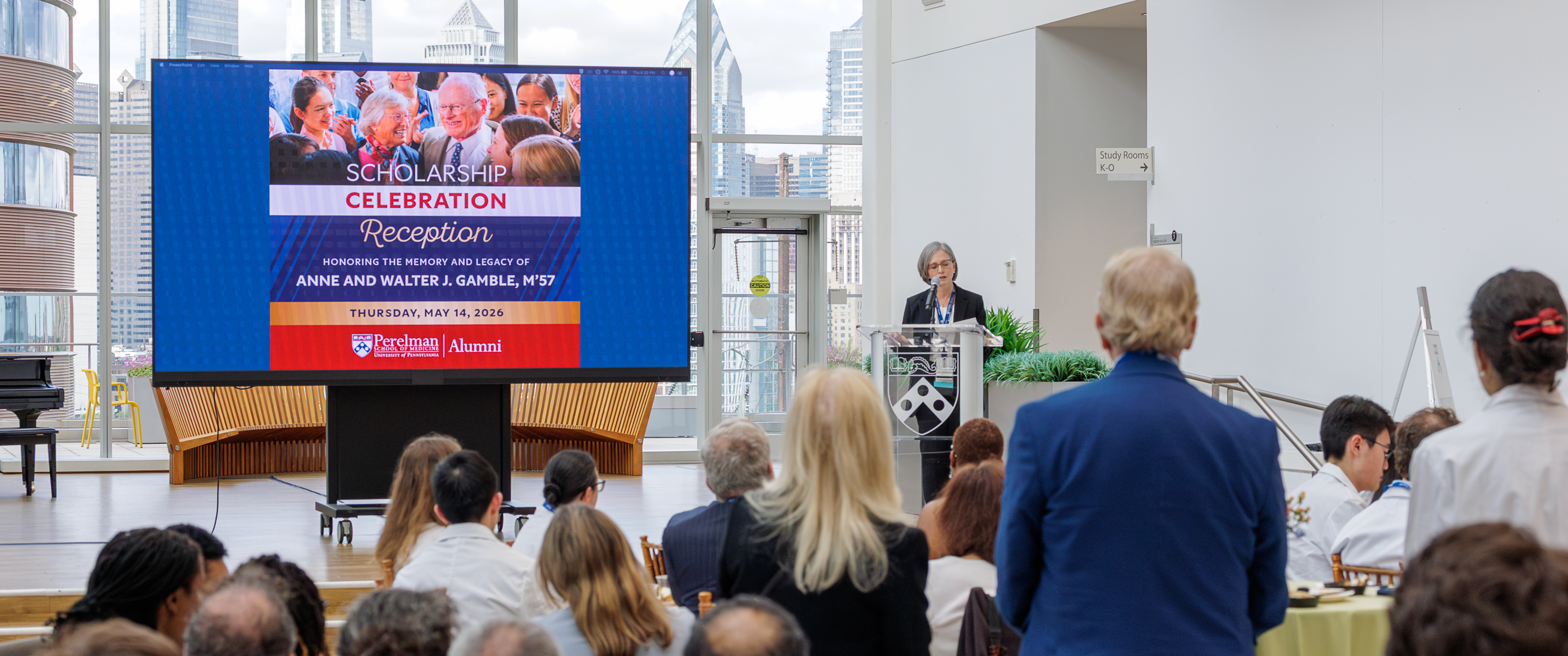 A group at the Jordan Medical Education Center looks to Jennifer Kogan, MD, on stage with a large image celebrating Walter and Anne Gamble’s legacy and scholarships