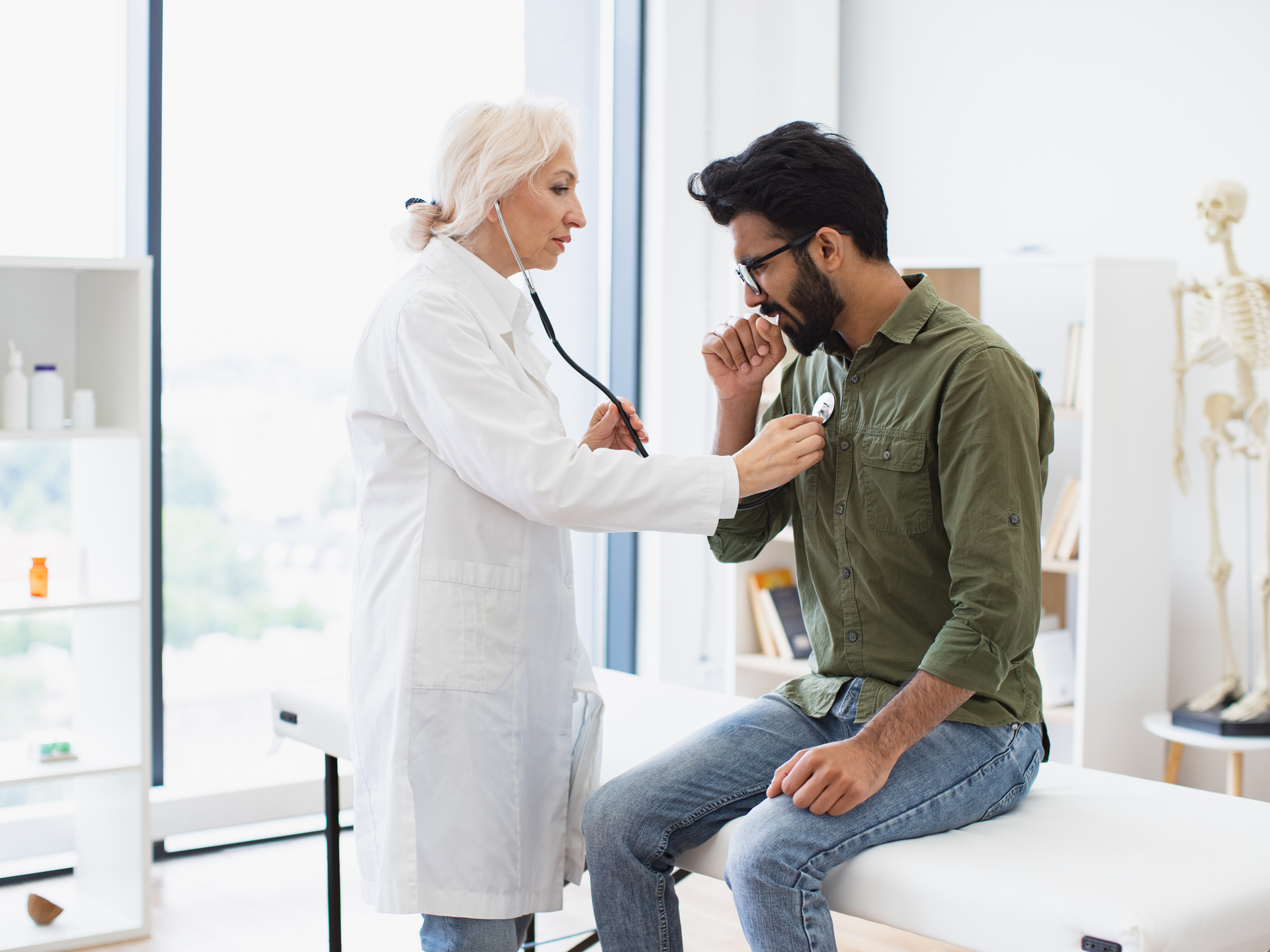 Doctor in white lab coat checking lungs and heart via stethoscope. 