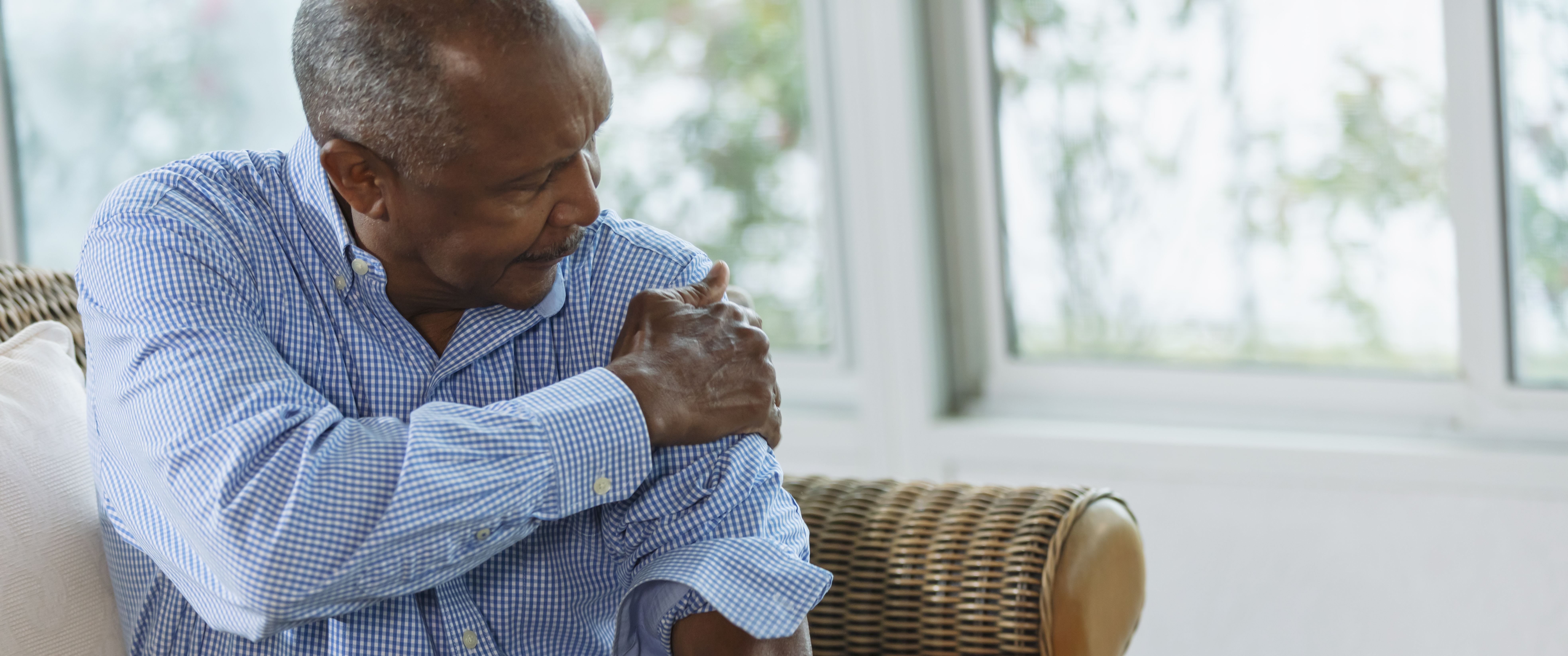 Black man sitting in chair grasping his shoulder