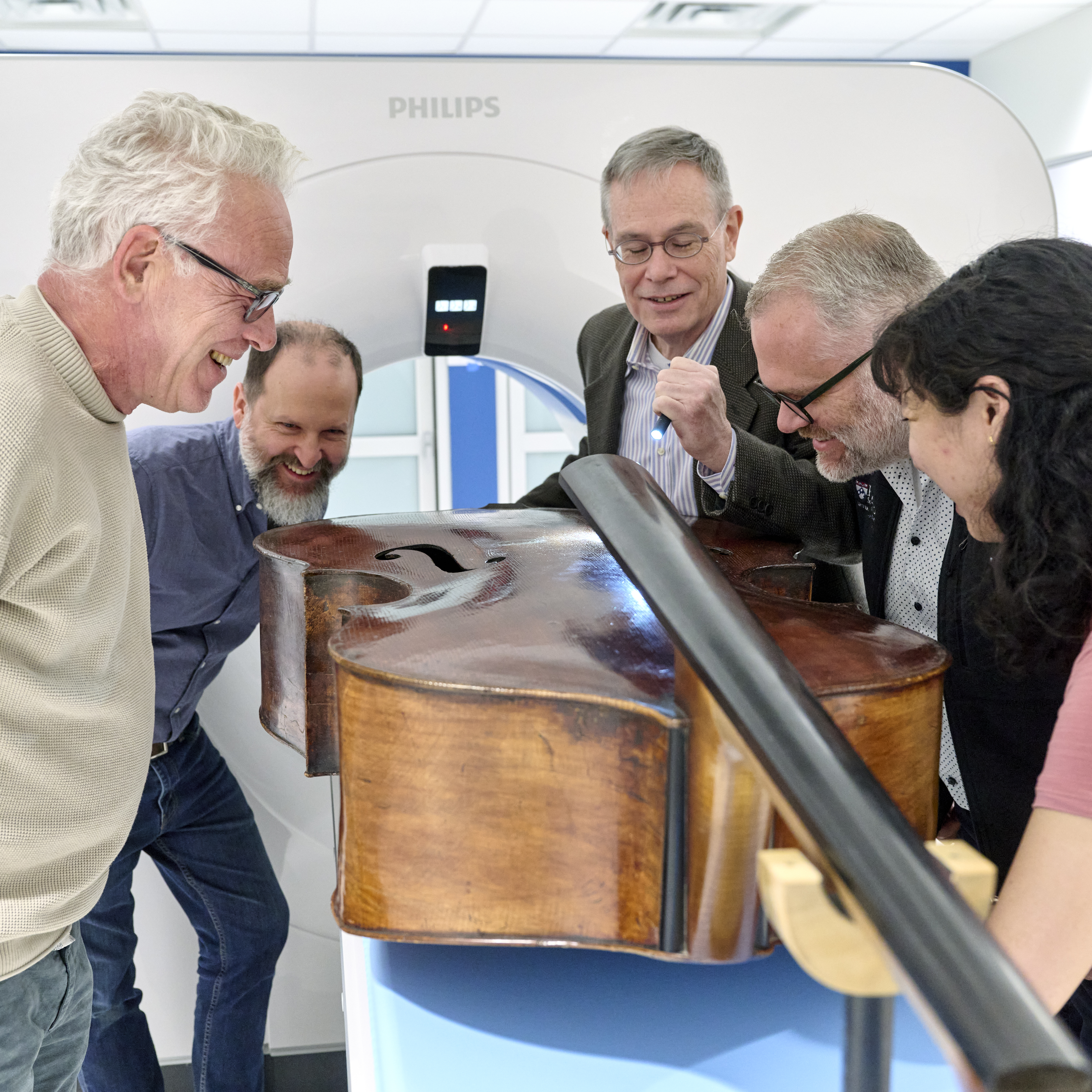 A team of scientists and music experts gathers around a double bass instrument beside a CT scanner