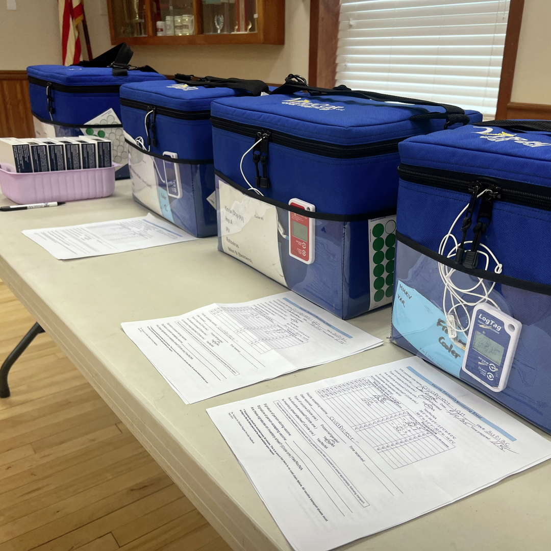 Blue containers holding vaccines, placed on a folding table within the fire hall vaccine clinic.