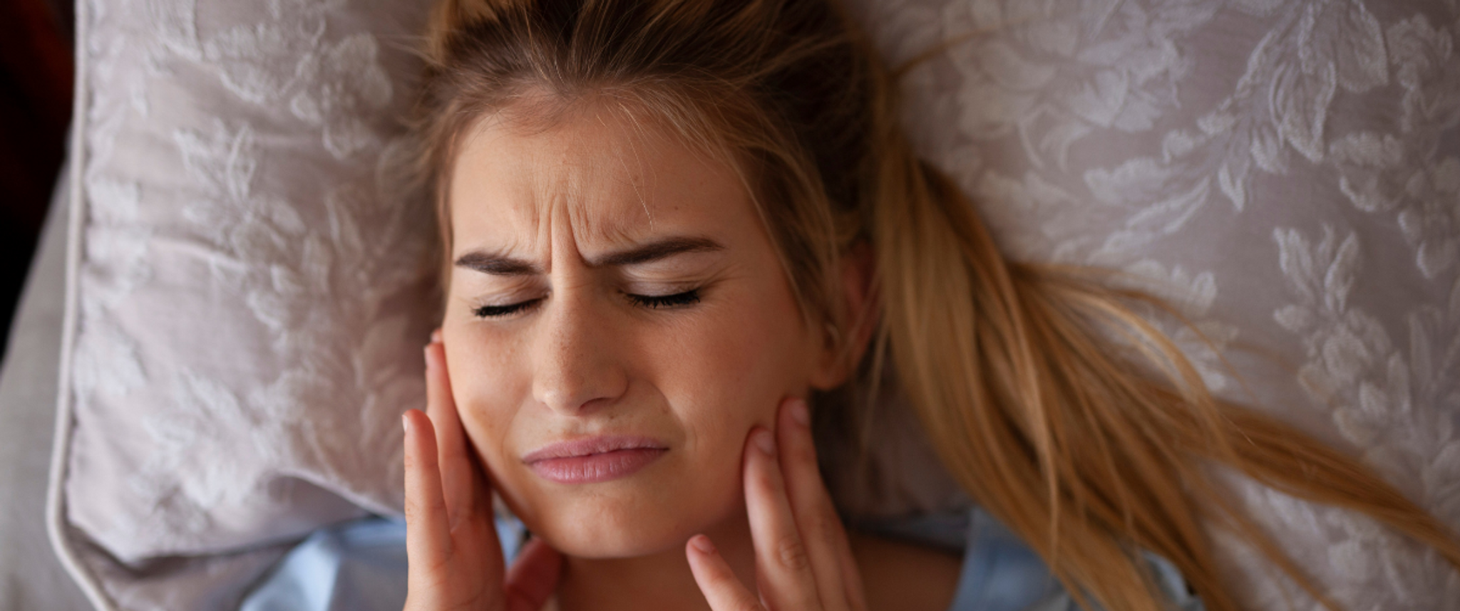Woman lying on pillow in pain with hands touching jaw